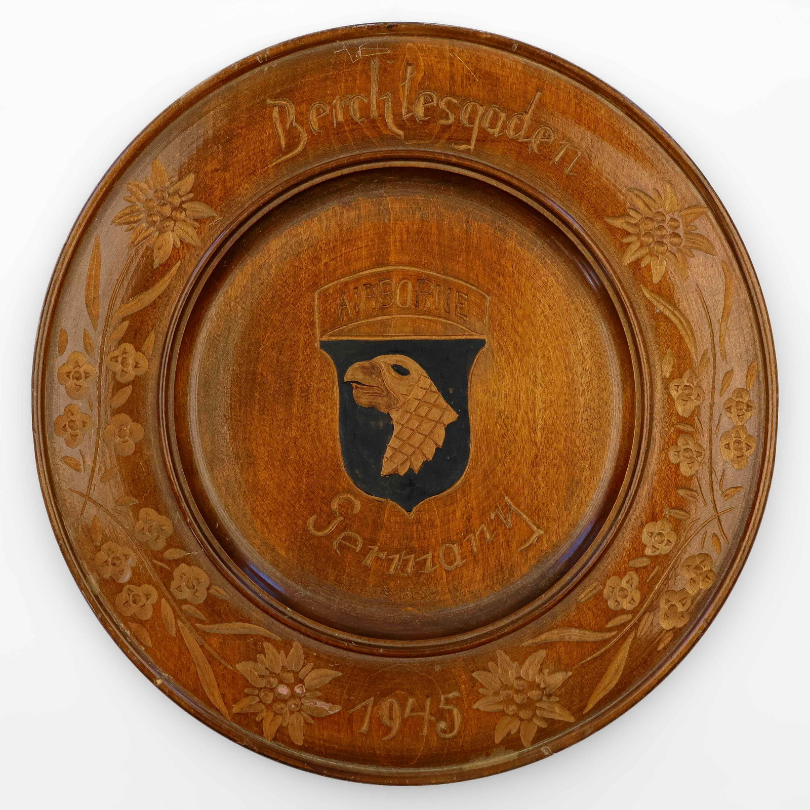 101ST AIRBORNE 'BERCHTESGADEN' CAPTURE SOUVENIR WOODEN PLATE: A rare relic honoring the historic capture of Hitler's Berchtesgaden retreat by the 101st Airborne on May 4, 1945. Likely carved by a craftsman in the town, the plate measures 10.5 in. in diameter and