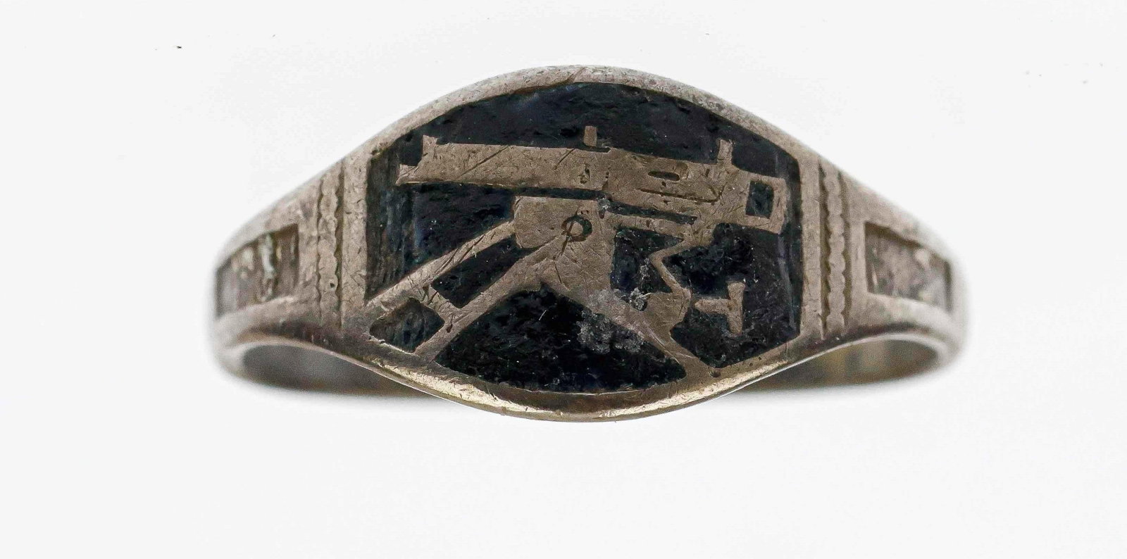 WORLD WAR I MACHINE GUNNERS RING: A scarce, small band ring featuring the insignia of a machine gun mounted on a tripod against a glossy black enamel background. Hallmarked ‘800’ for silver content on the interior. A tiny 