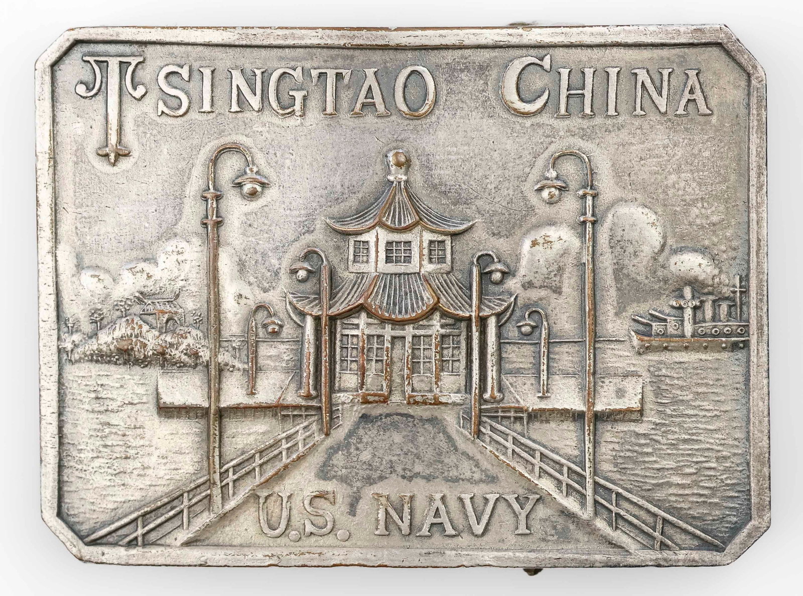 WORLD WAR I U.S. NAVY TSINGTAO BELT BUCKLE: Scarcely seen World War I U.S. Navy belt buckle for a navy man serving in Tsingtao, China. Metal construction with a silver finish, 2.25 x 1.5 in., bearing an embossed image of a dock, with the text: 