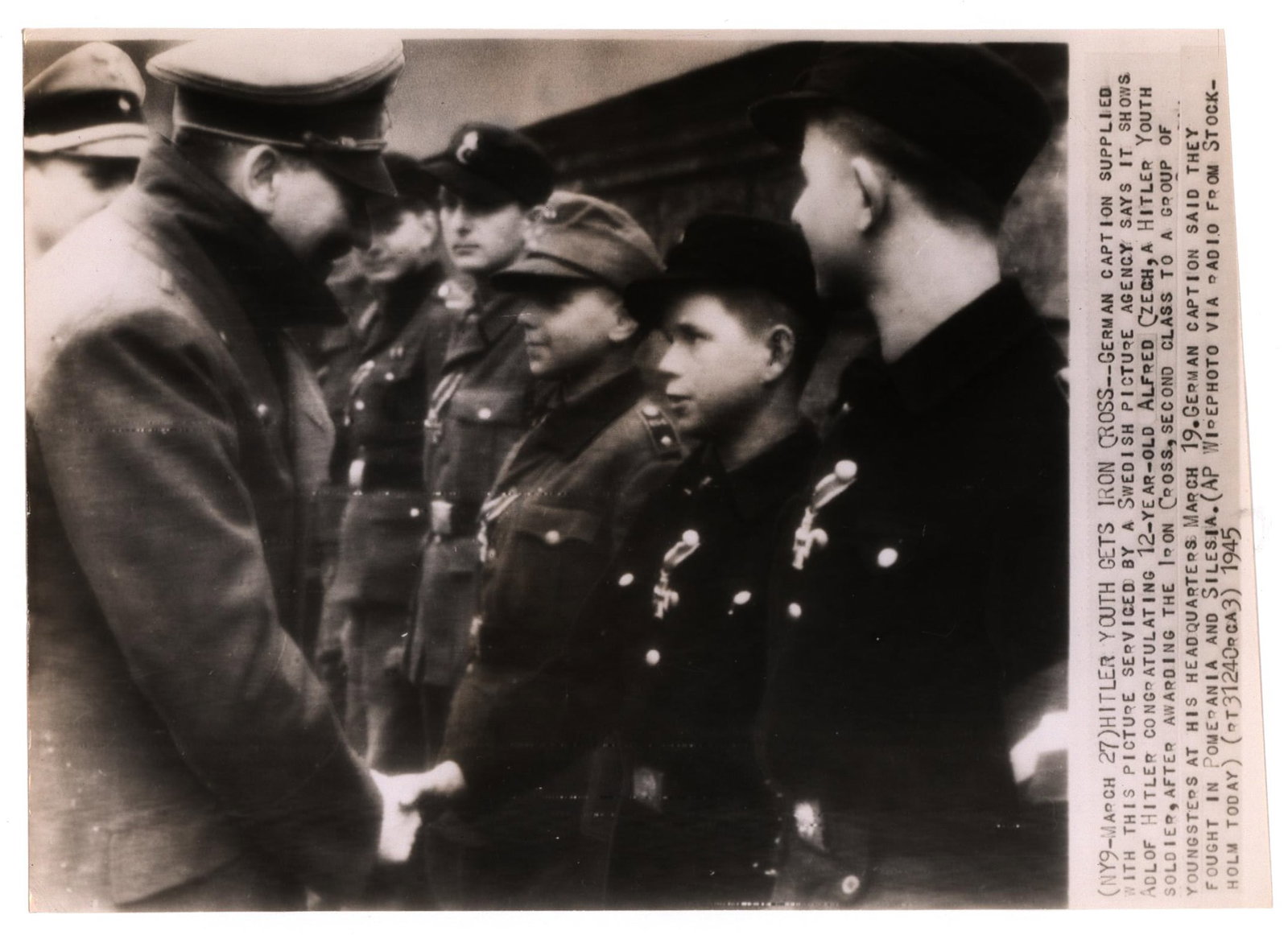 THE LAST PHOTOGRAPH OF ADOLF HITLER: Rare period press photograph, 10 x 7.25 in. b/w, an A.P. Wirephoto showing the last known image of Adolf Hitler while at the Chancellery as he awards members of the Hitler Youth with Iron Crosses for 