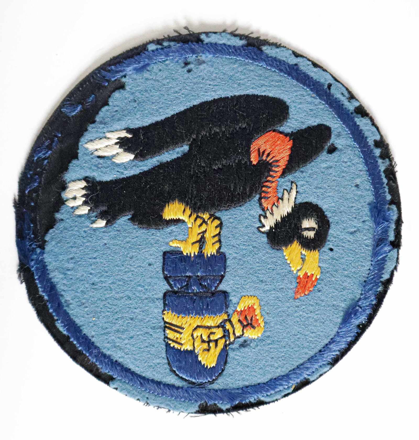 USAAF VULTURE PATCH WITH BOMB: An original World War II USAAF 'vulture' patch, measures 5 in. dia. embroidery on wool, showing a black vulture perched over a swastika-festooned bomb. Bears moth holes and wear at the edges, likely f