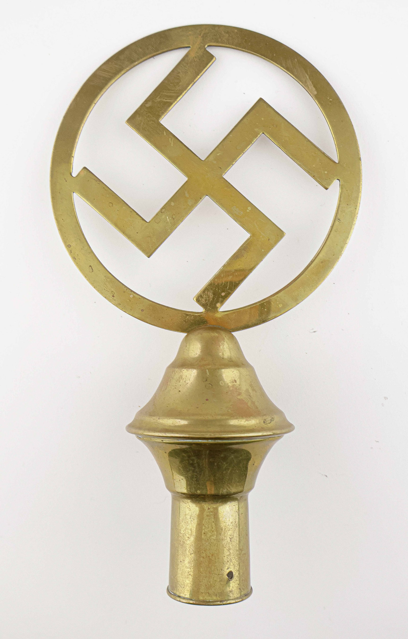 THIRD REICH BRASS FLAGPOLE TOPPER: German Third Reich brass flagpole topper, displaying a one-piece mobile swastika within a circle, attached to a two-piece clamshell base for attaching to a wooden pole, with one hole for an attachment