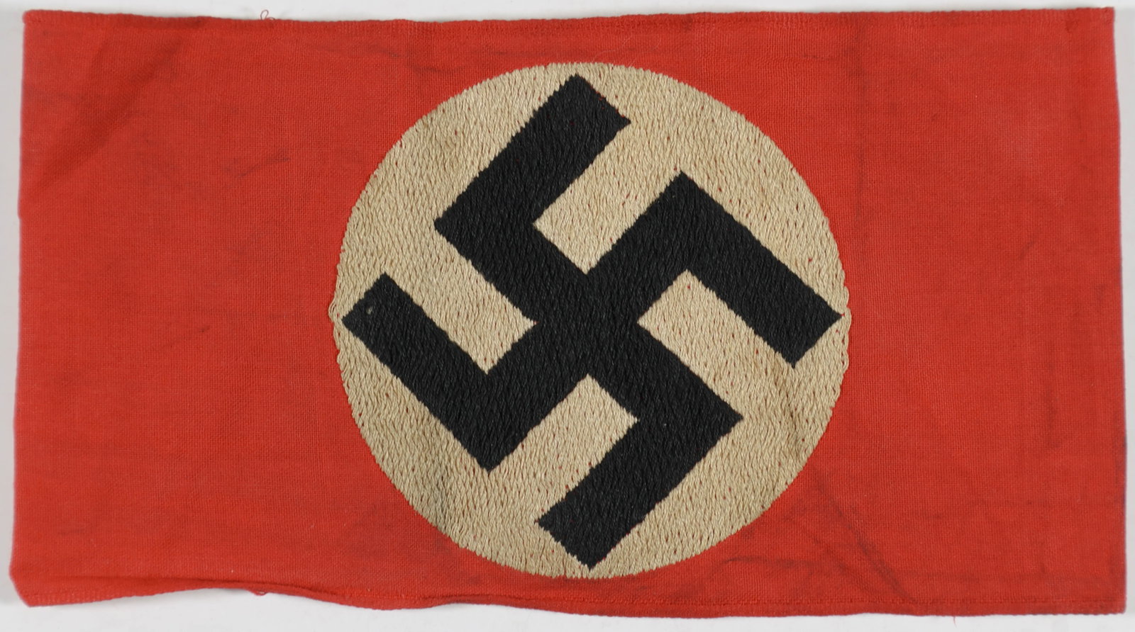 NSDAP ARMBAND: Original red cotton armband of an NSDAP party member, 6.5 in., sewn together at the ends. The face bears a clamp-dyed black swastika on a white disc. No markings. A bit soiled, else very good.