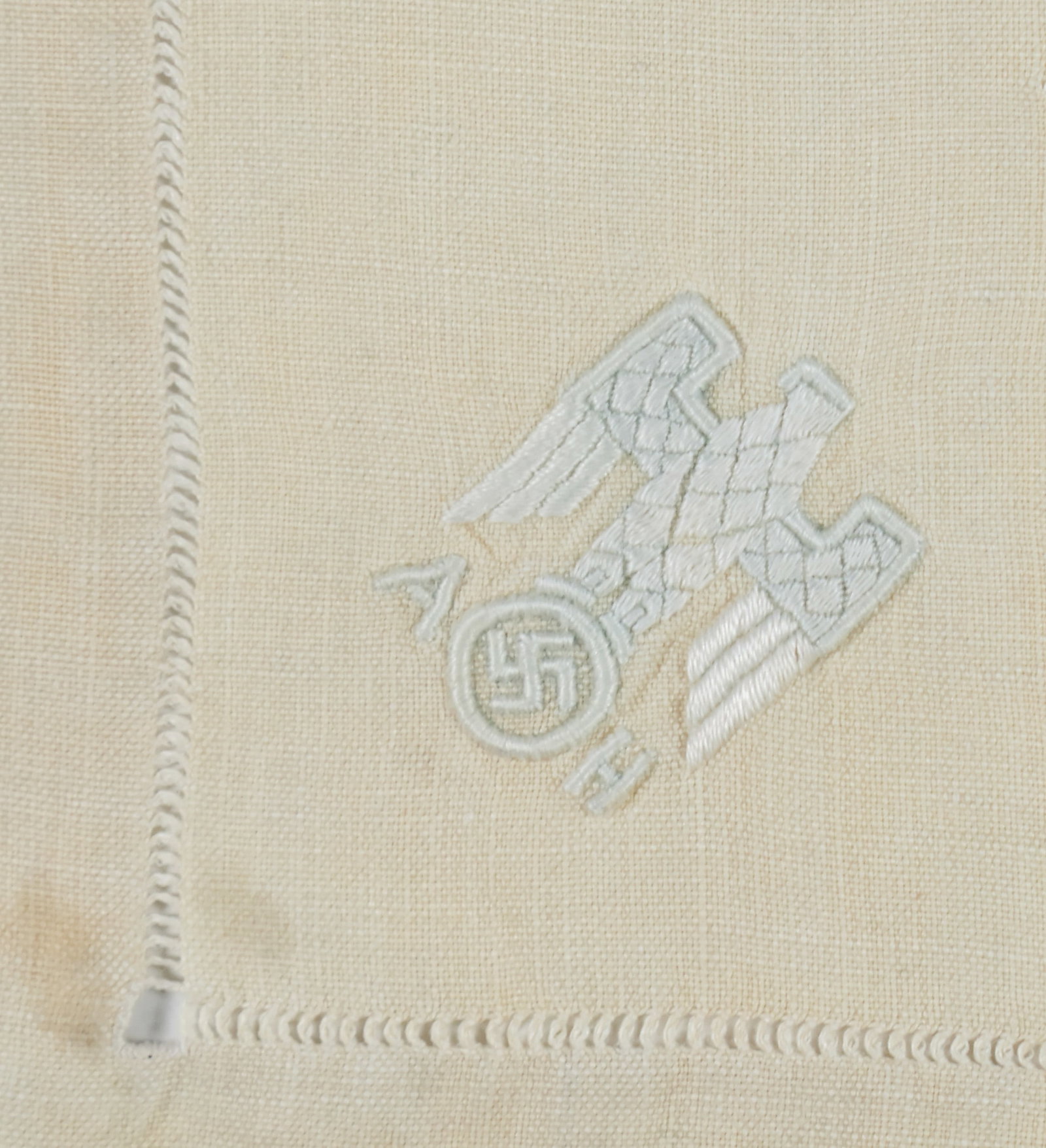 ADOLF HITLER INFORMAL TABLE NAPKIN: A beige linen informal pattern table napkin owned by Adolf Hitler, measures approx. 12 x 12 in. square, bearing an embroidered Nazi eagle device and his initials 'AH' in white satin thread. Fine condi