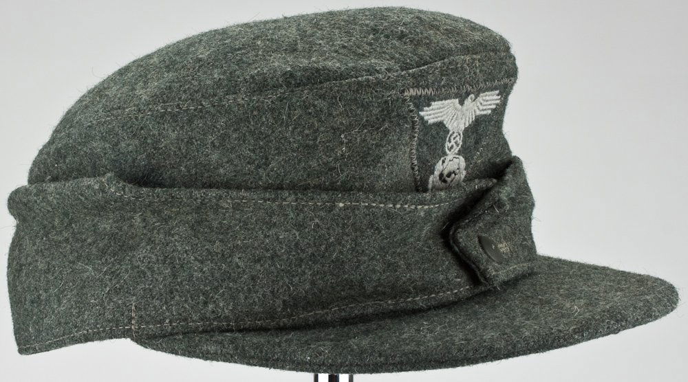 WAFFEN-SS M43 WINTER CAP: Scarce Waffen-SS M43 winter cap, coarse green wool with two metal button flap, similar wool eagle and totenkopf patch sewn to front of cap at the time of manufacture. The sides of the interior lining