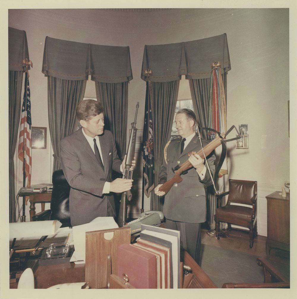 (JOHN F. KENNEDY): Two fine photos of Kennedy taken during his administration, the first 8" x 8" color showing Kennedy and an unknown general in the Oval Office, Kennedy holding an M-16 while the general holds a modern