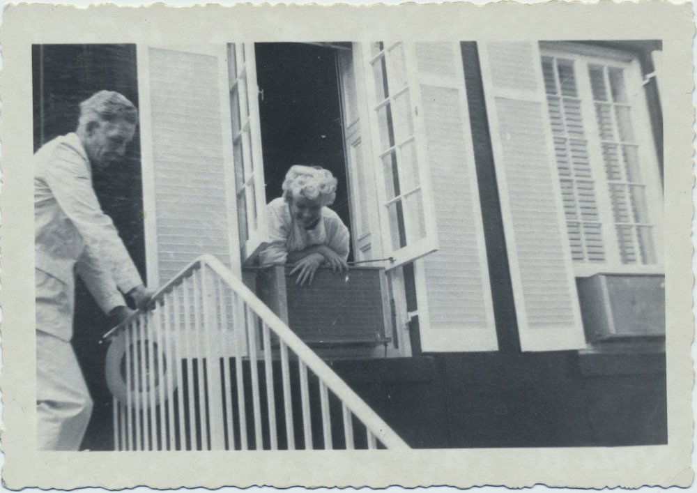 MARILYN MONROE ORIGINAL PHOTOGRAPH: Original candid photograph of Marilyn Monroe from the set of "The Seven Year Itch" depicting Monroe smiling as she leans out of a second floor window, her arms crossed atop an air conditioner. A man i