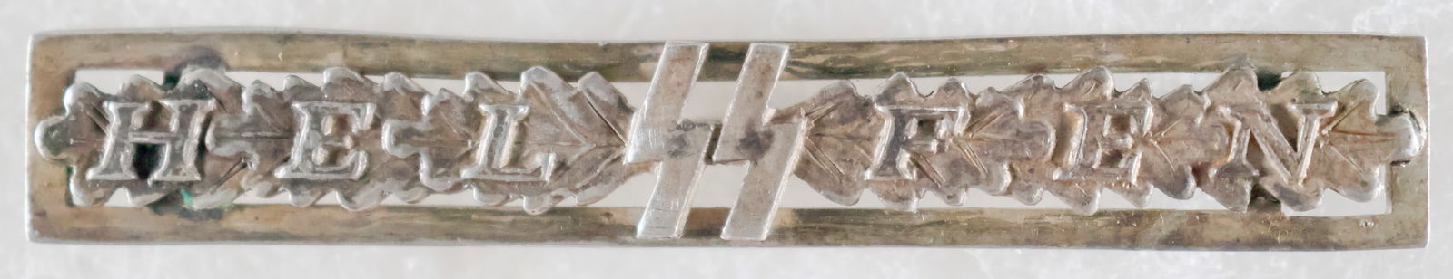 SS WOMEN'S AUXILLIARY 'HELFEN' CLASP: Solid silver badge, 2.25 x .25 in. displaying the 'sig' runes of the SS at center with the title 'Helfen' ('Helper), all over a band of oak leaves. The reverse is fitted with a horizontal hinged pin w