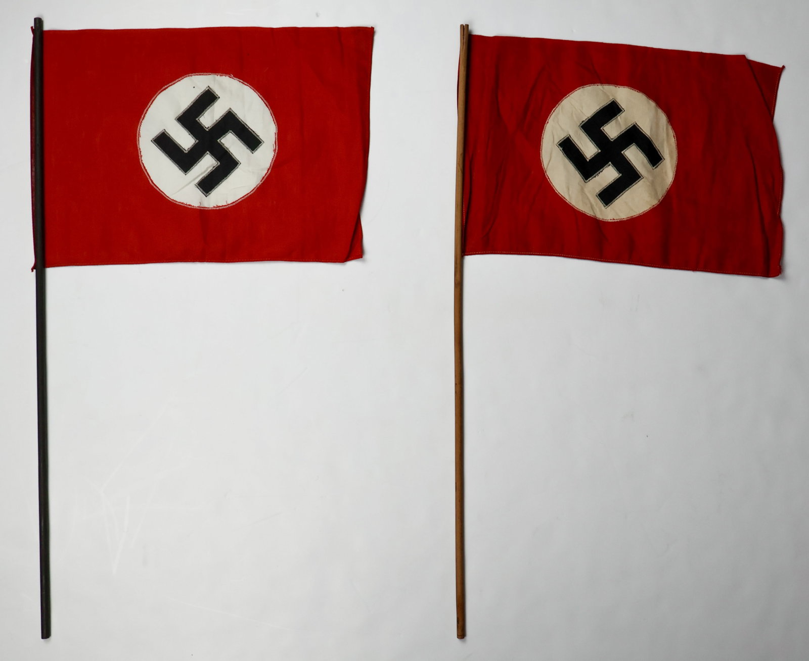 AMERICAN BUND SWASTIKA FLAGS (2): A fine pair of flags with the swastika and white circle sewn into a hole on a red background, both tacked to small wooden poles. These flags are associated with a German-American Bund chapter founded 
