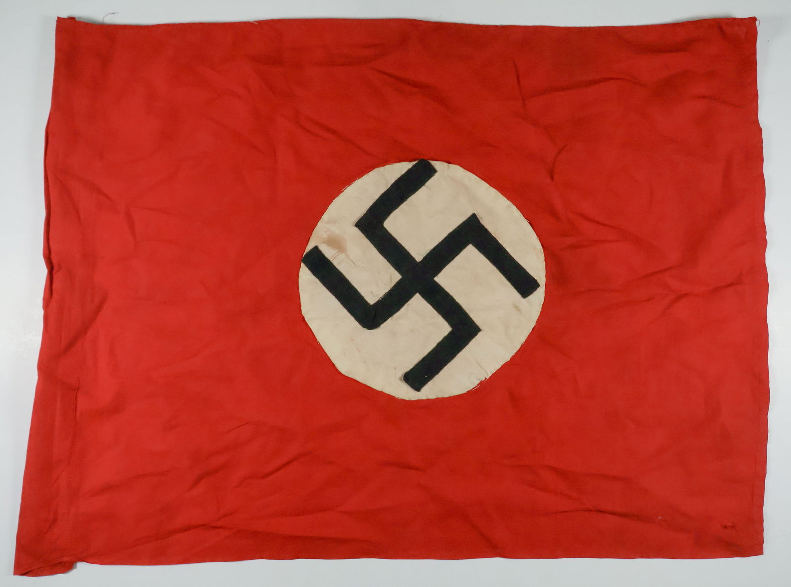 NAZI HOMEMADE PARTY CAR FLAG: A small homemade Nazi Party ersatz car flag 12 in. x 9 in., made of red dyed cotton with a hand-sewn swastikas on white roundels. Pole pocket present. Soiled, otherwise good.