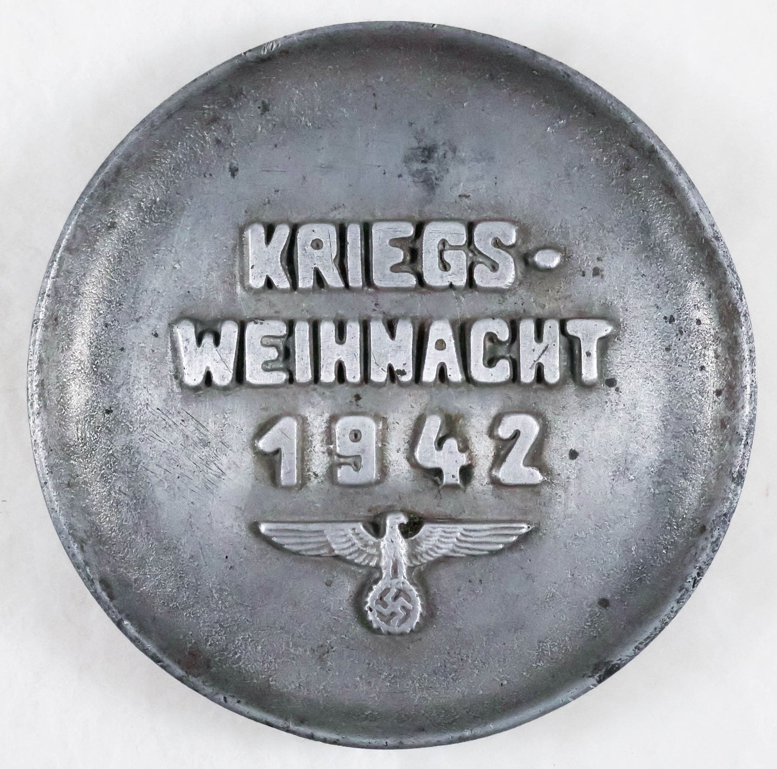 KRIEGSWEIHNACHT 1942 ALUMINUM PLATE: A well-made aluminum plate with silver finish, 7.75 in. dia. The plate bears the message: ‘KRIEGSWEIHNACHT 1942’ ('War Christmas 1942') along with a national eagle. On the reverse is the m