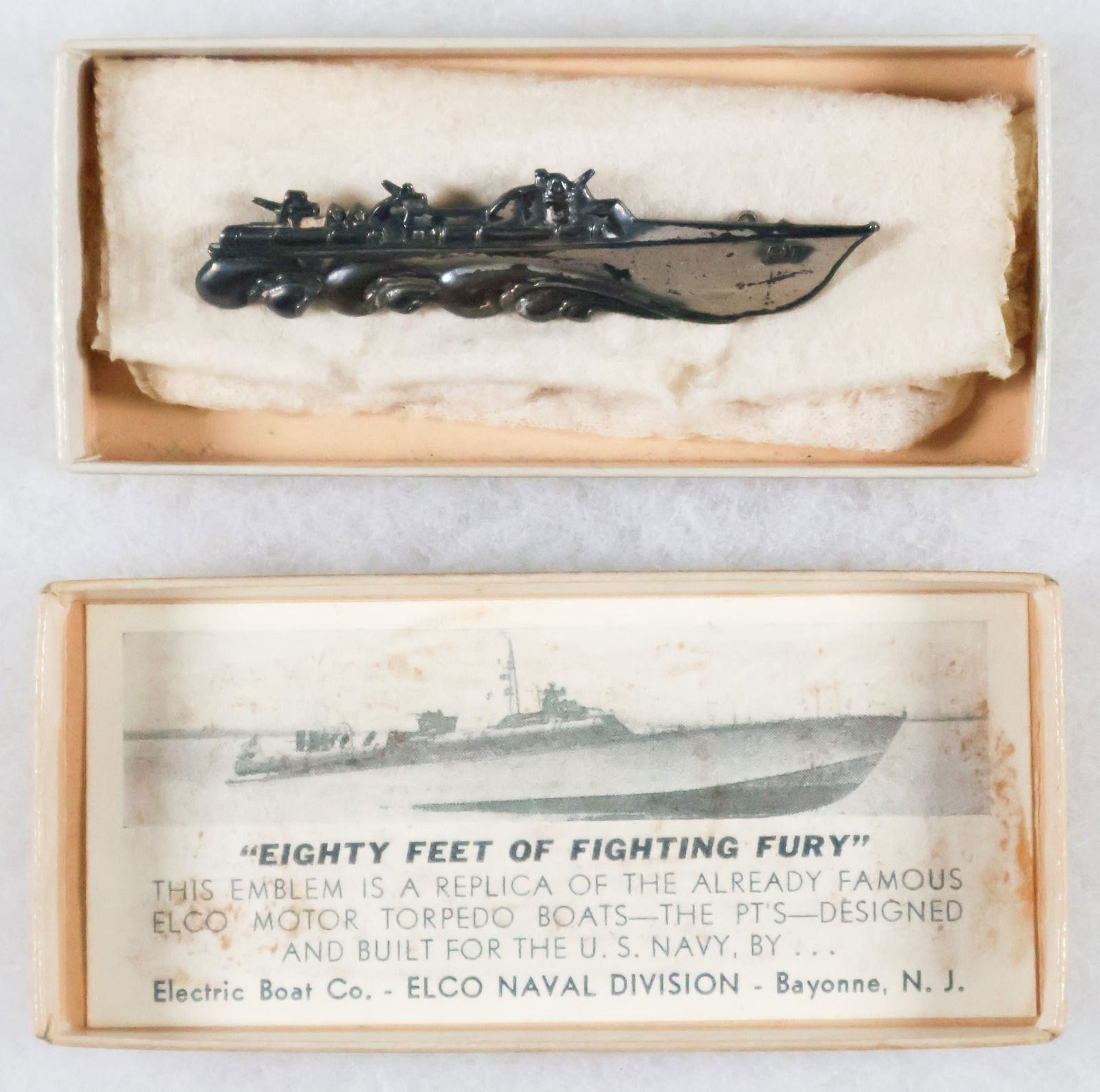 PT-BOAT BADGE FROM ELCO: A scarcely seen original silver-plated PT-boat badge, 2.75 x .5 in., a replica of a PT-boat as it is racing through the sea. The reverse has the Elco company emblem and the patent number. The badge co