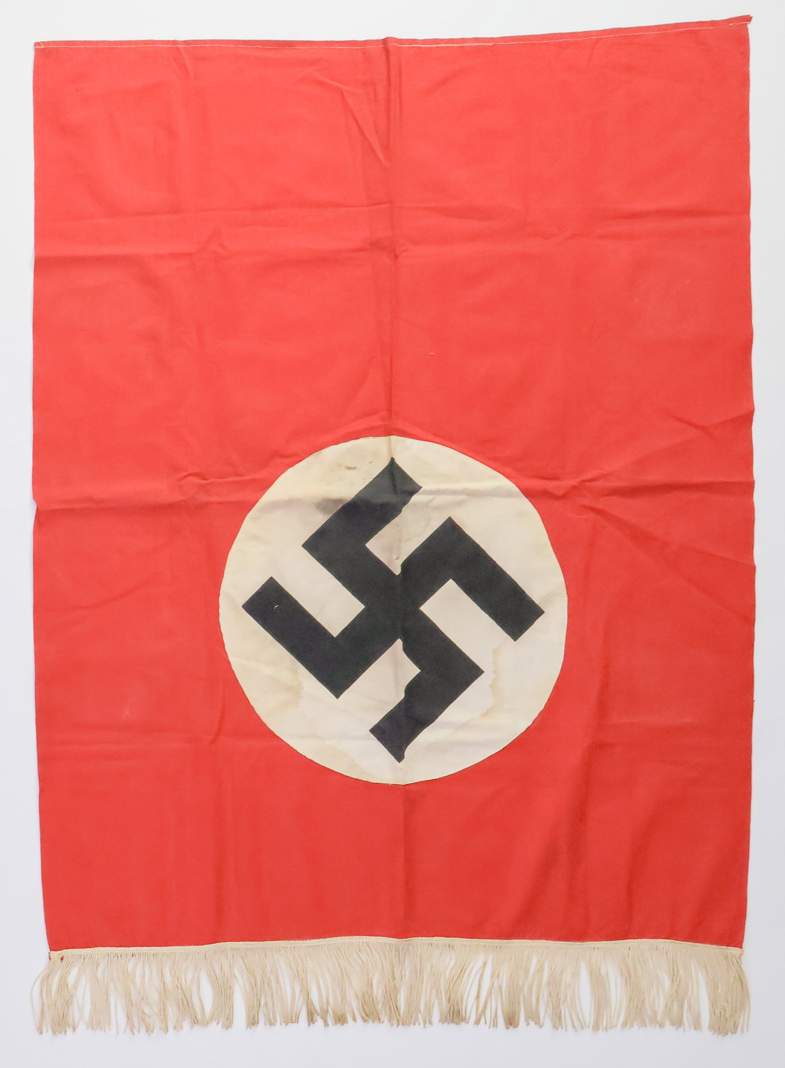 NSDAP PODIUM BANNER: NSDAP one-sided podium banner, 29.5 x 37.75 in., with a sewn-on printed swastika on a white roundel, which in turn is applied to the large red field of the banner. The bottom of the banner bears a ful
