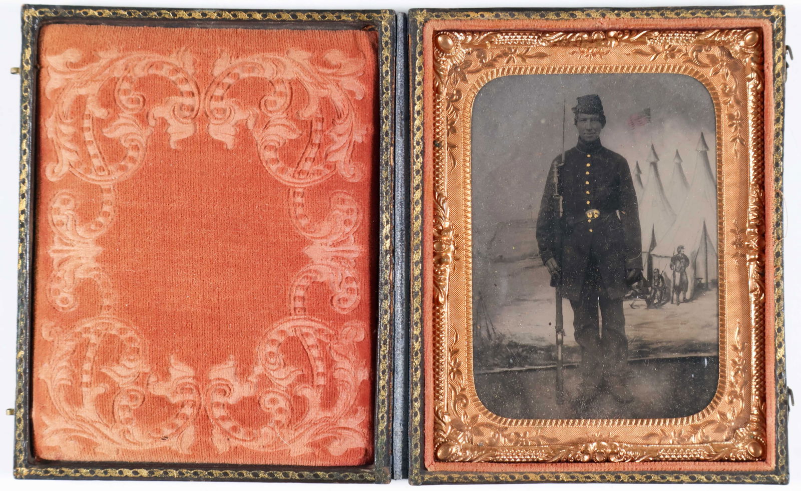 TINTYPE OF A UNION SOLDIER: A superb tintype in original velvet-lined leather case, shows a Union soldier in uniform, bayoneted rifle at the ready and with a backdrop of tents on a battlefield. The image measures 2.25 x 3.25 in.