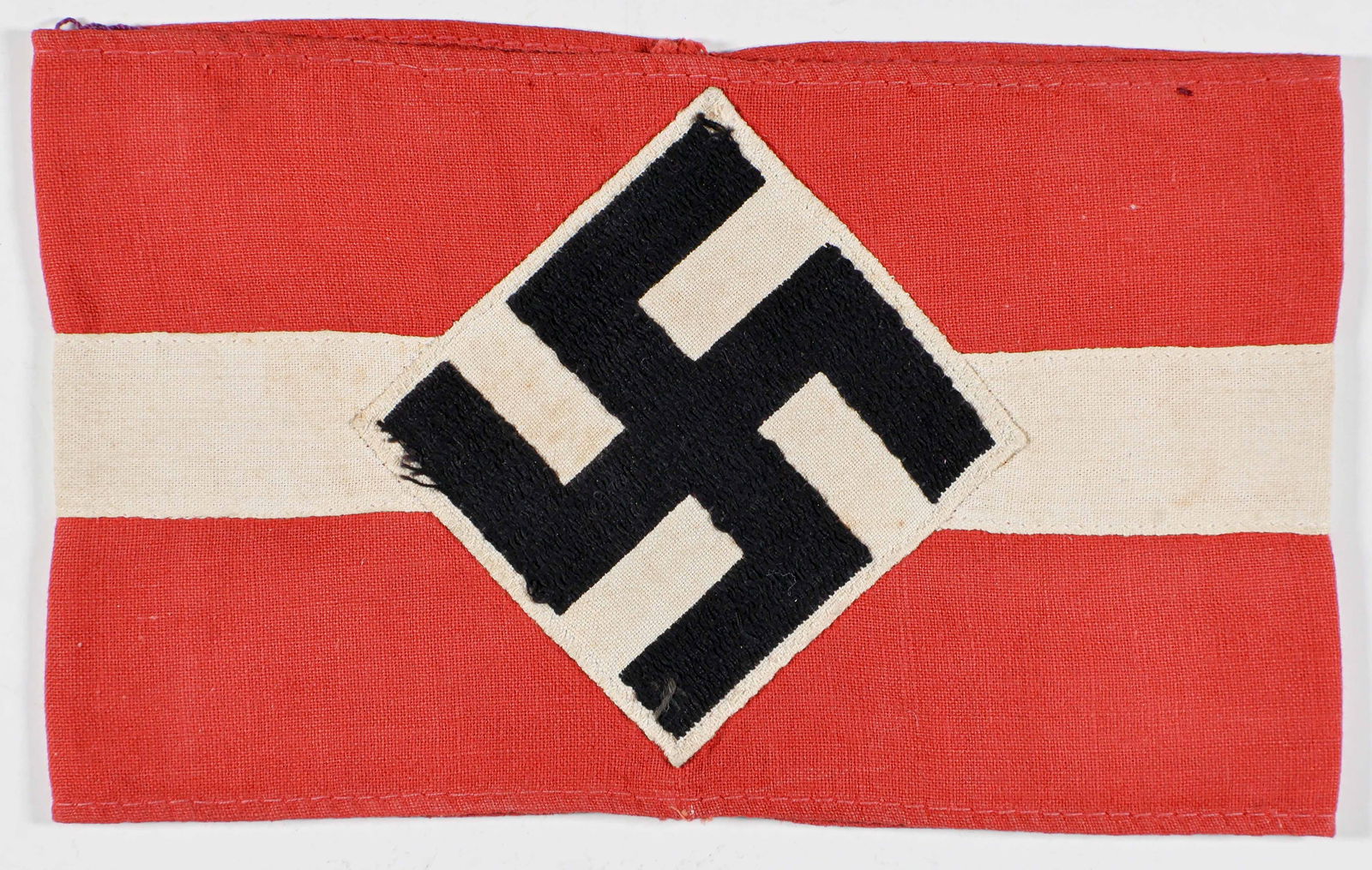 HITLER YOUTH ARMBAND: Red cotton Hitler Youth armband, 13 x 4 in., bearing a white applied band, with a BeVo-style embroidered mobile swastika in the center. Sewn at the ends, shows some minor soiling overall, else very go
