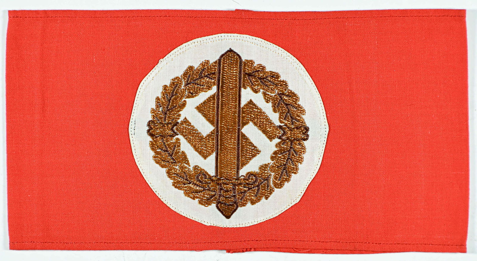 S.A. SPORTS ARMBAND: S.A. Wehrmannschaft sports armband worn by participants in S.A. sports competitions, 17 x 4 in. red cotton with embroidered sword, oak leaves and swastika, joined at rear. With paper RZM tag within. V