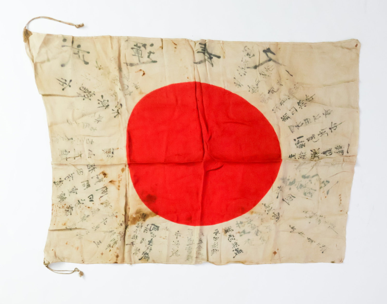 JAPANESE ‘GOOD LUCK’ FLAG: A 31.5 x 22.5 in. Japanese ‘Good Luck’ flag made of silk with an oddly oblong sun in the center. Surrounding the sun are untranslated kanji wishing the owner luck in battle. Soiled, otherwise fine