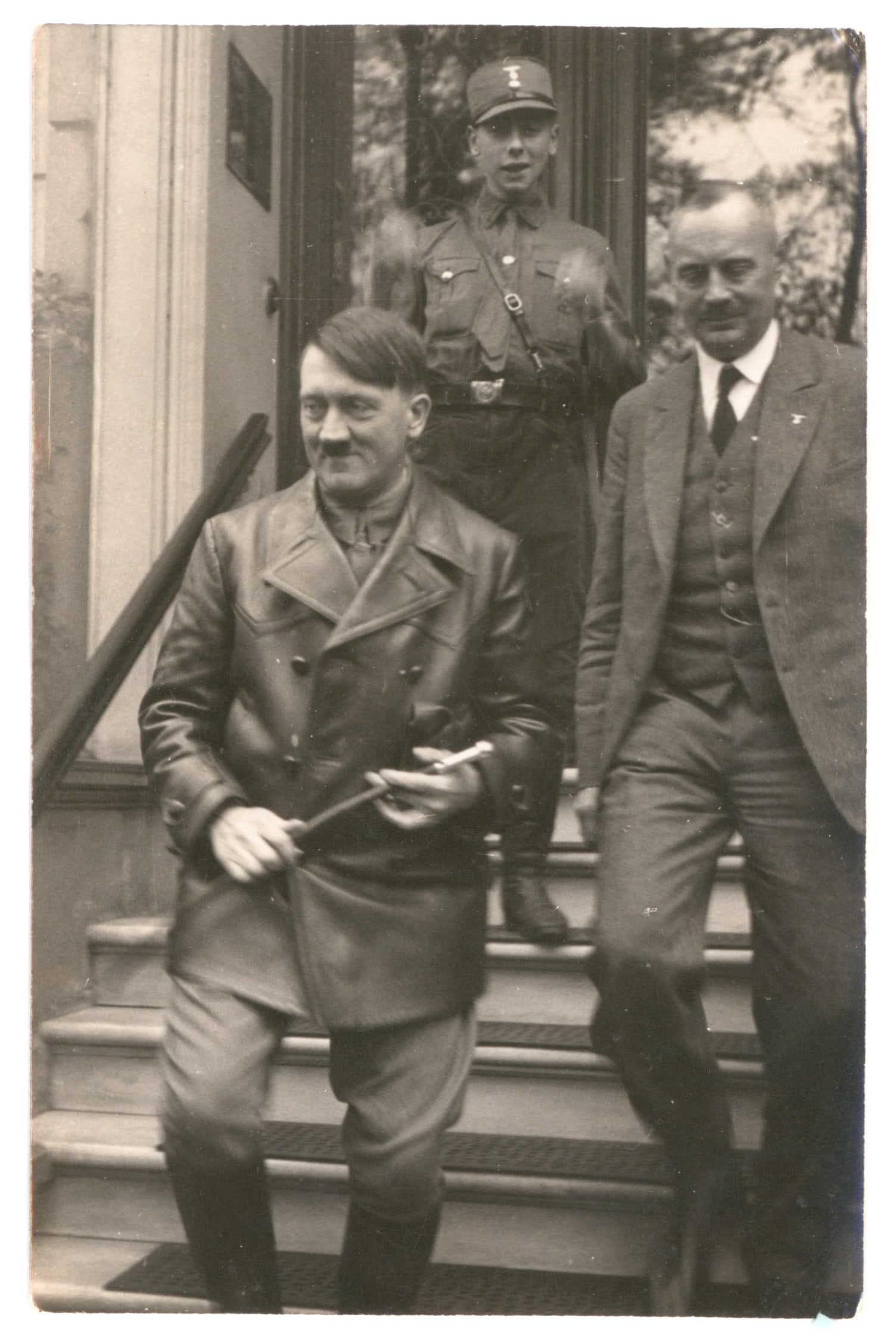 (ADOLF HITLER): A real-photo post image of Hitler, 3.5 in. x 5.5 in. b/w, showing the Fuhrer in 1921 exiting a building with another gentleman. Identified on verso as Bremen, Oct. 29, 1932. Tiny mounting traces to co