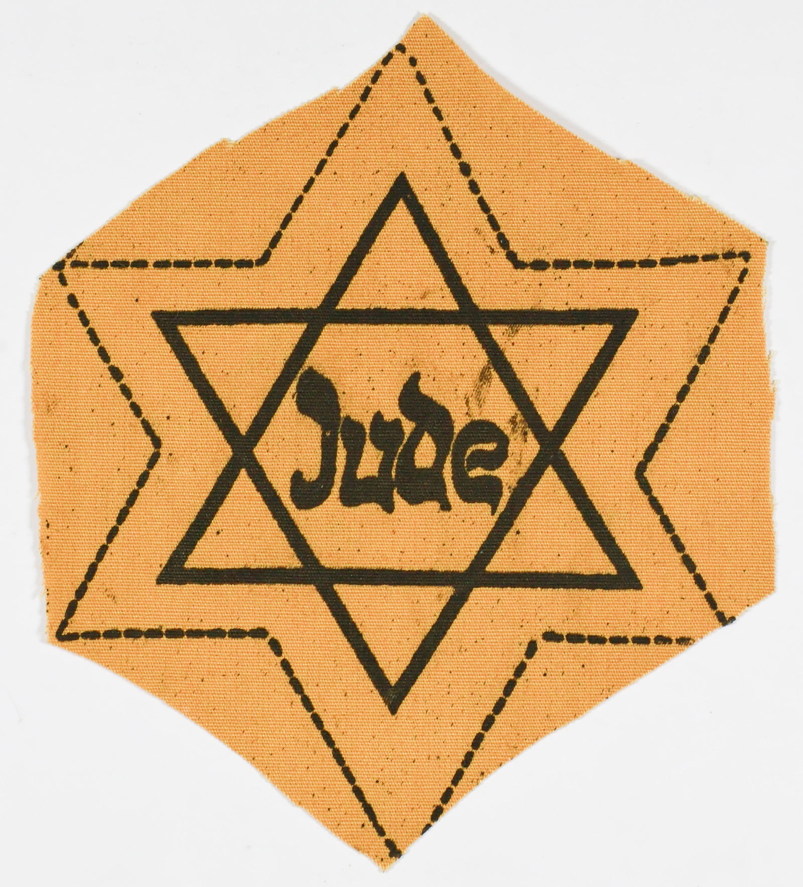 ‘JUDE’ STAR OF DAVID: Yellow cloth Star of David imprinted 'Jude', 3.5 in. diameter, in correct yellow cloth color and weave, very heavily printed in black with some smudging to ink. This example is unused and is likely