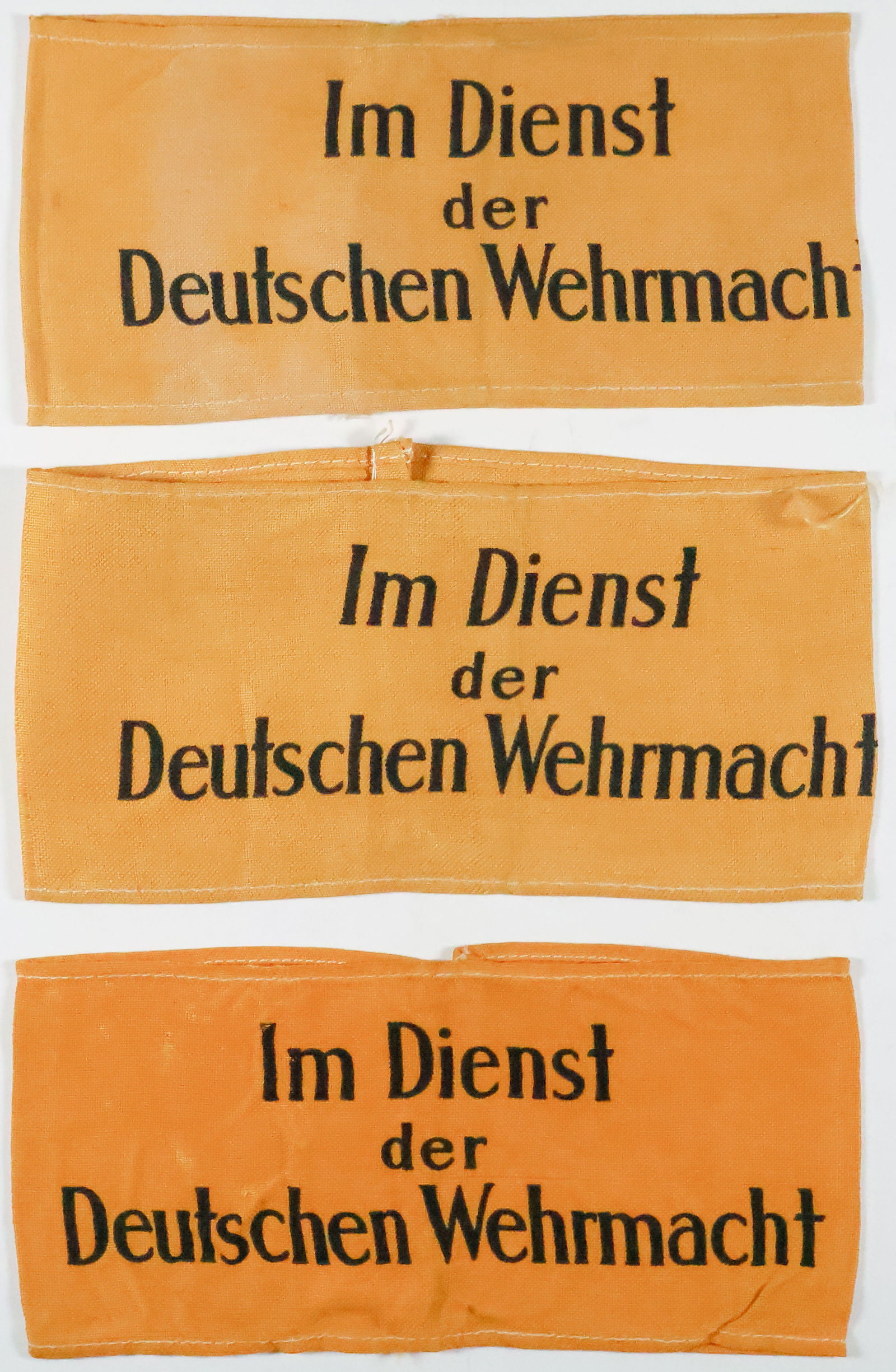 ‘IM DIENST DER DEUTSCHEN WEHRMACHT’ ARMBANDS (3): Lot of three yellow cotton armbands, each approx.15 x 4 in., joined at the rear and bearing the black text: ‘Im Dienst der Deutschen Wehrmacht’ (‘In The Service Of The German Armed F
