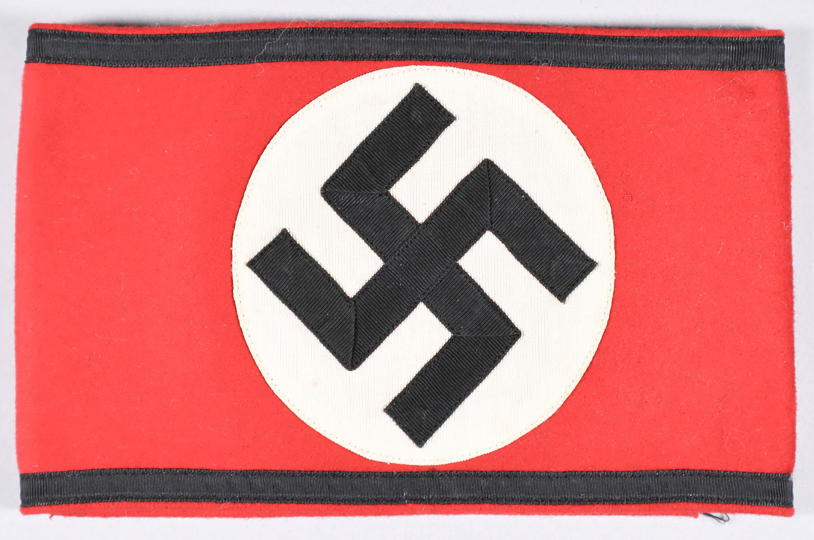 SS ARMBAND: SS armband, 20.5 x 4.5 in., red wool construction with a separate ribbed white circular field and folded black swastika sewn thereon, the folds not sewn down. Black ribbed tresses sewn to the top and