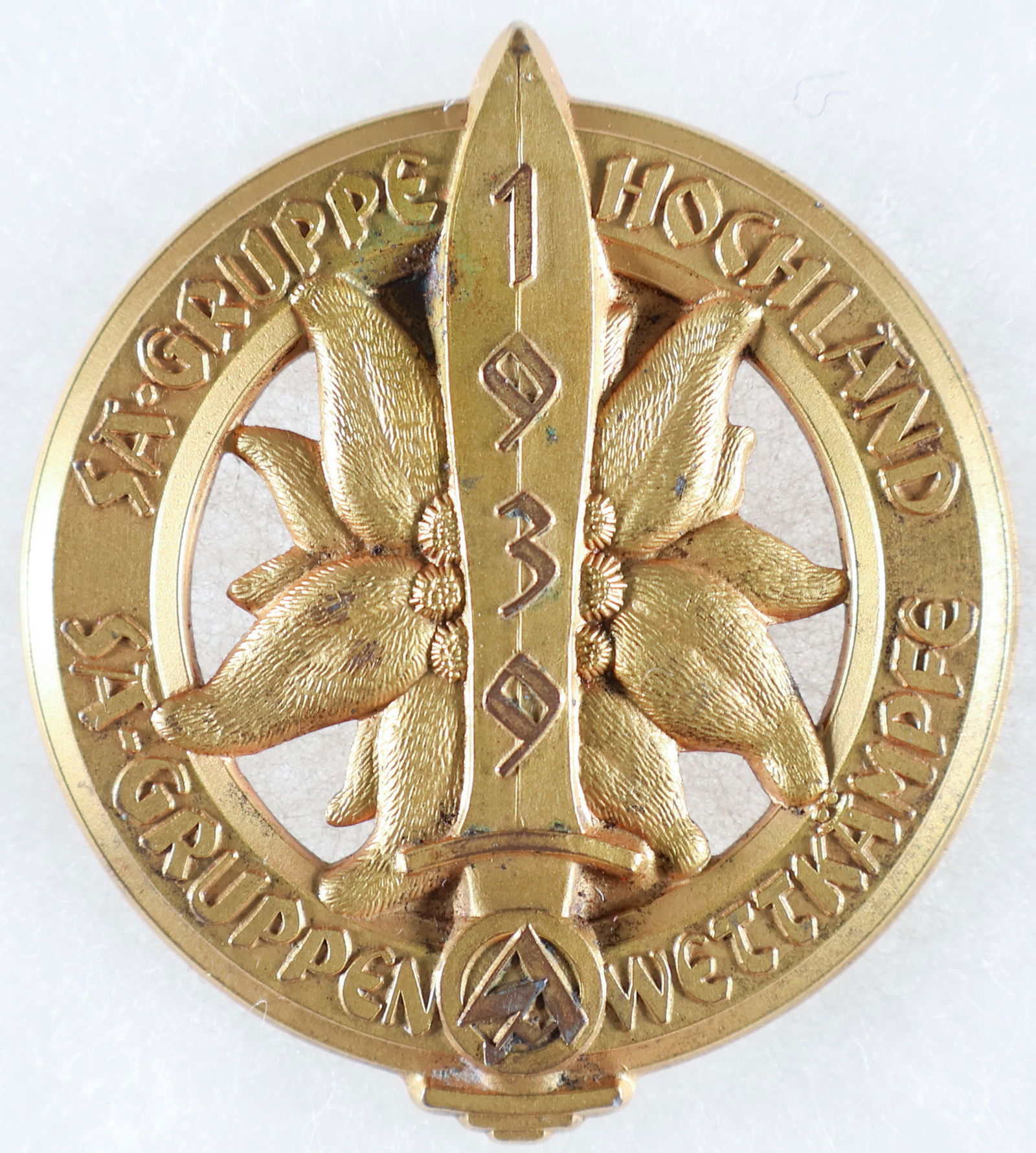 SA-GRUPPE HOCHLAND TABLE MEDAL: Scarce sports competition table medal from a tinnie, 55mm x 50mm, from SA Gruppe Hochland, depicting a sword atop an edelweiss with an SA emblem on its handle and the year '1939,' on the blade. The