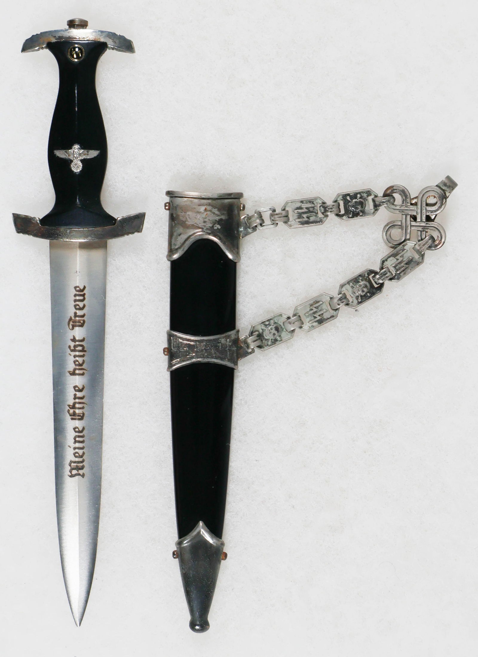 MINIATURE SS DAGGER: Miniature chained SS dagger with scabbard, 7.25 in. long, engraved and darkened steel blade, inset emblems in the wood grip, painted metal scabbards, and all metal fittings. Very good.