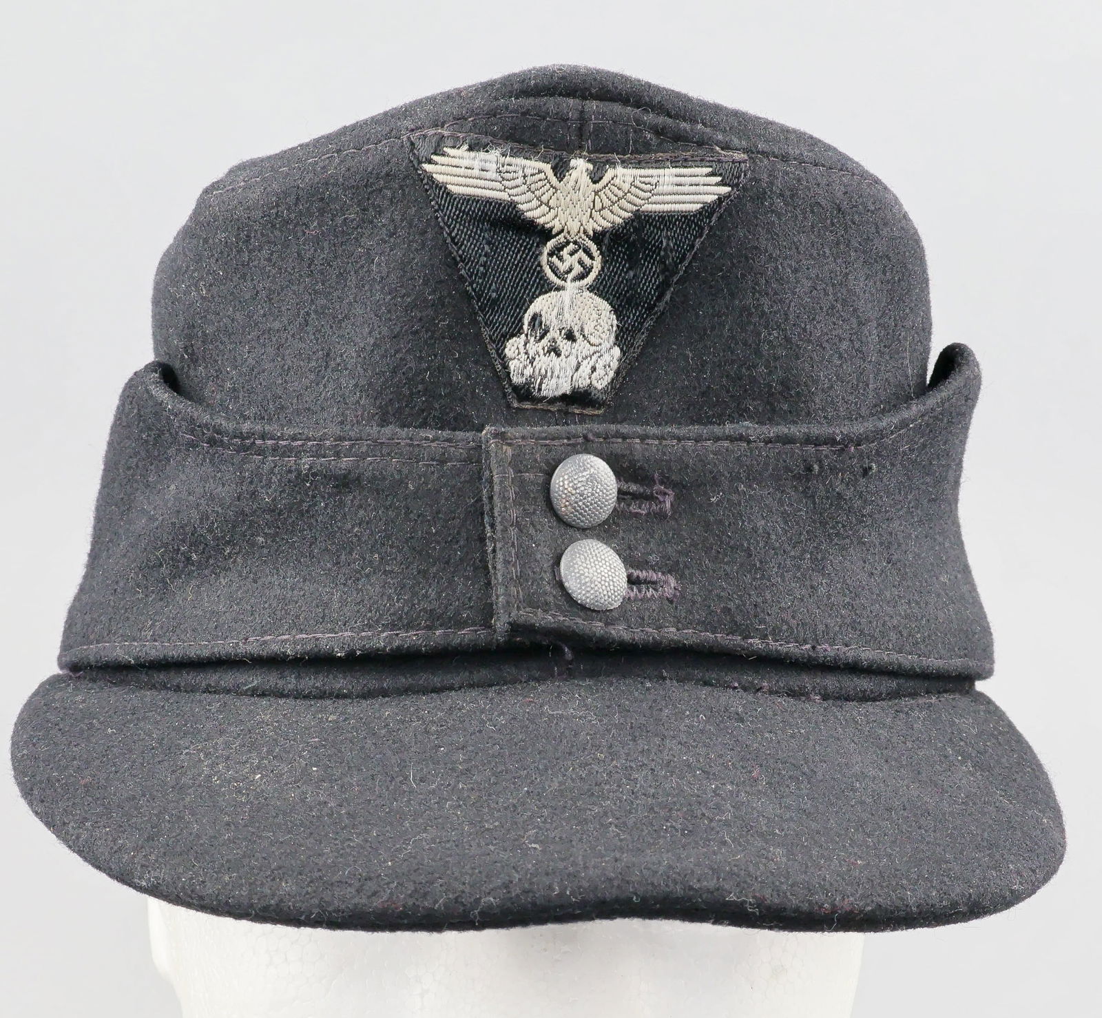 WAFFEN-SS M43 ENLISTED PANZER CAP: A Waffen-SS M43 Panzer enlisted man’s cap of later black wood/rayon mixture construction, with tan cotton lining size marked ‘57’. Shows a machine embroidered trapezoid SS eagle and