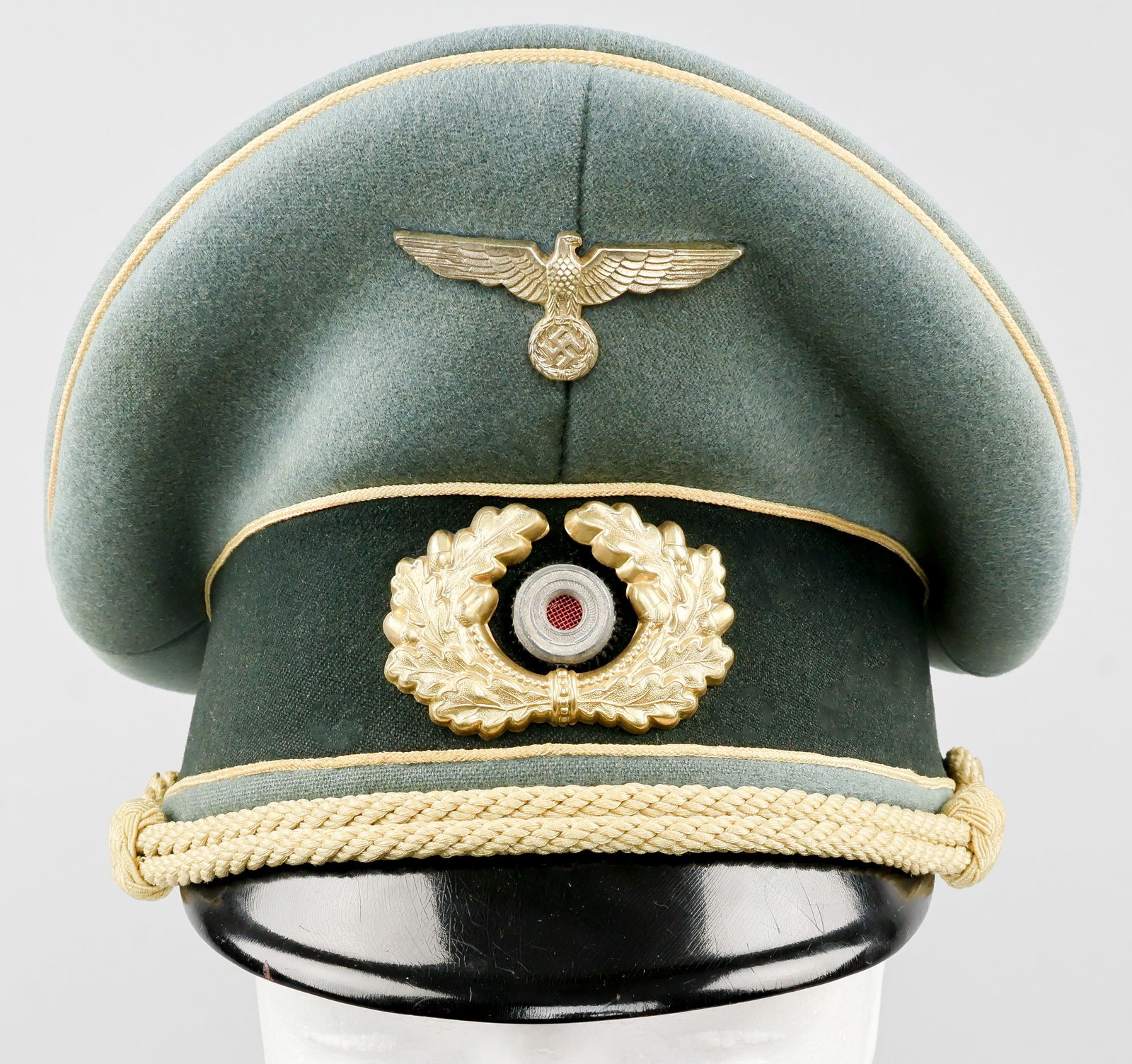 NAMED WEHRMACHT GENERAL OFFICER’S CAP BY EREL: A fine example of a Wehmacht General Officer’s visor cap, constructed of greenish-gray wool in a high peaked ‘saddle’ shape, over a band of very dark green wool, with a black vulkanf
