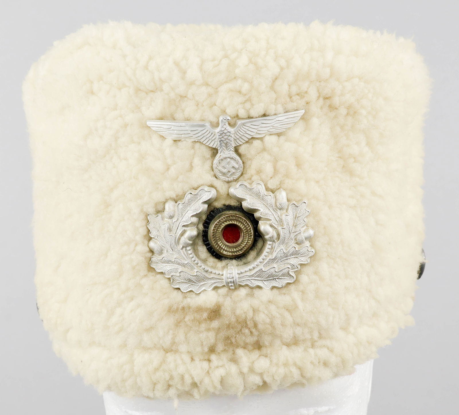 WEHRMACHT COSSACK CAVALRY CORPS FUR CAP: A very rare article of Third Reich headgear, a round white fleece visorless cap, fitted with a metal shell national eagle badge over a metal and wool national tricolor cockade, surrounded by a