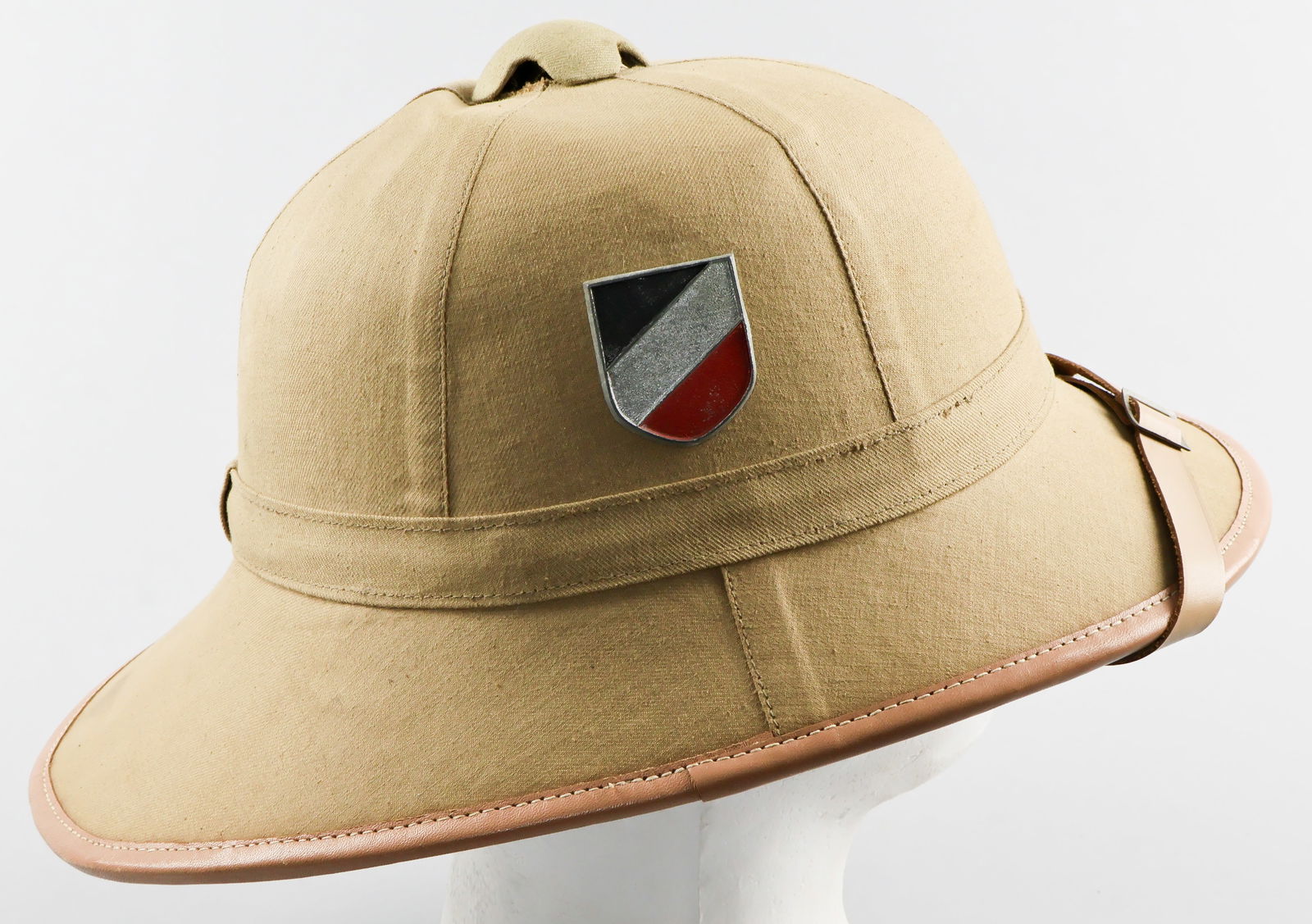 LUFTWAFFE TROPICAL PITH HELMET: A Luftwaffe personnel pith helmet, the exterior covered with khaki cotton and with tan leather brim and chin strap. The left-hand side is fitted with a zinc Luftwaffe eagle insignia, while the right