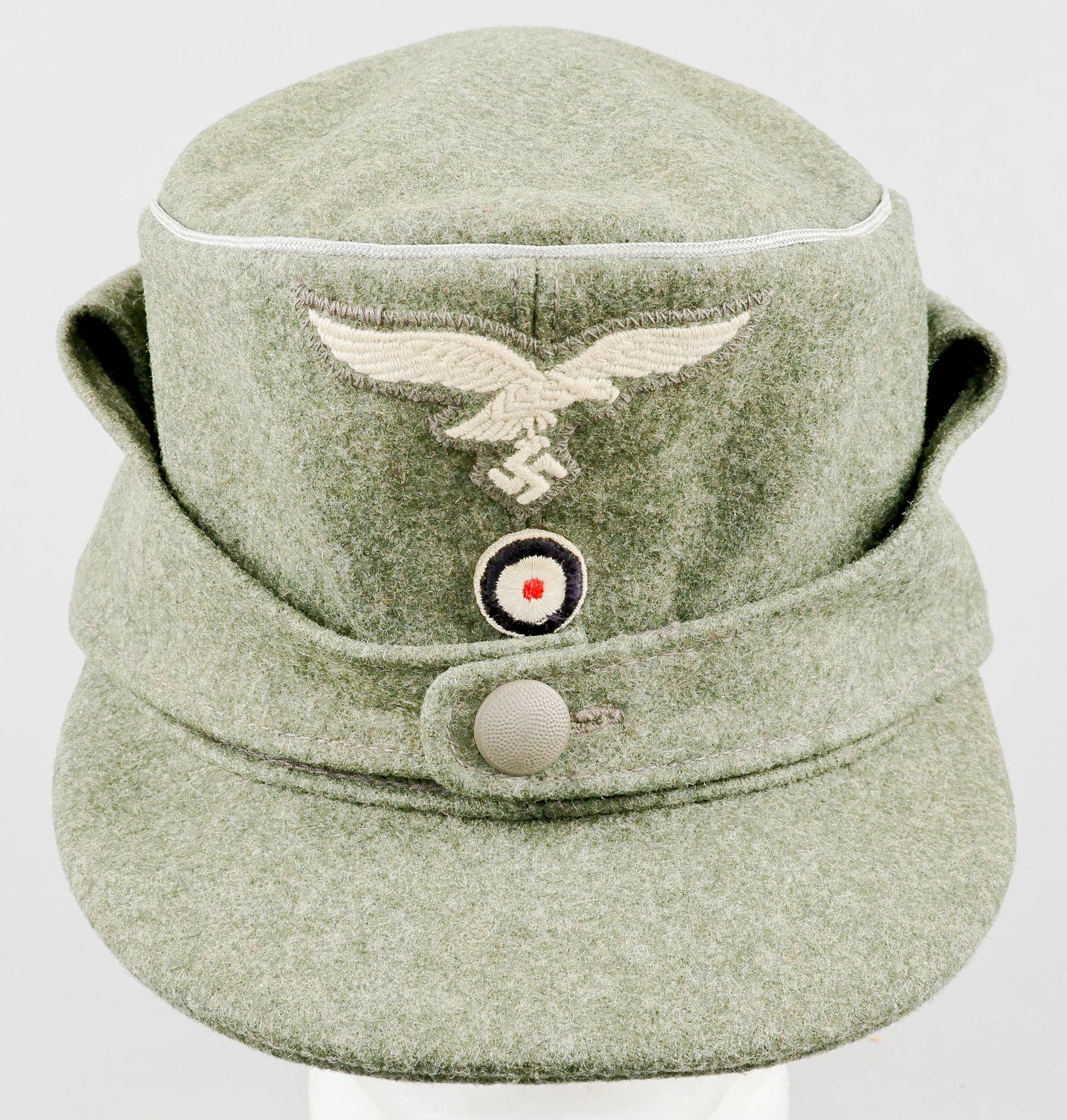 LUFTWAFFE OFFICER’S M43 FIELD CAP: Luftwaffe officer’s M43 field cap, constructed of grey wool. A Luftwaffe eagle insignia in white thread embroidered on gray wool is sewn to the peak, above an embroidered roundel. The crown is