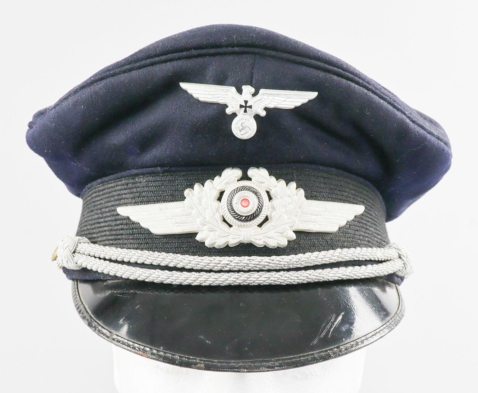 LUFTWAFFE VETERAN OFFICER'S VISOR CAP: Luftwaffe officer's visor cap issued to veterans of service in the Luftwaffe, a lightweight navy blue wool peaked cap with a woven black side band. Shows typical Nazi-era veteran's national eagle and