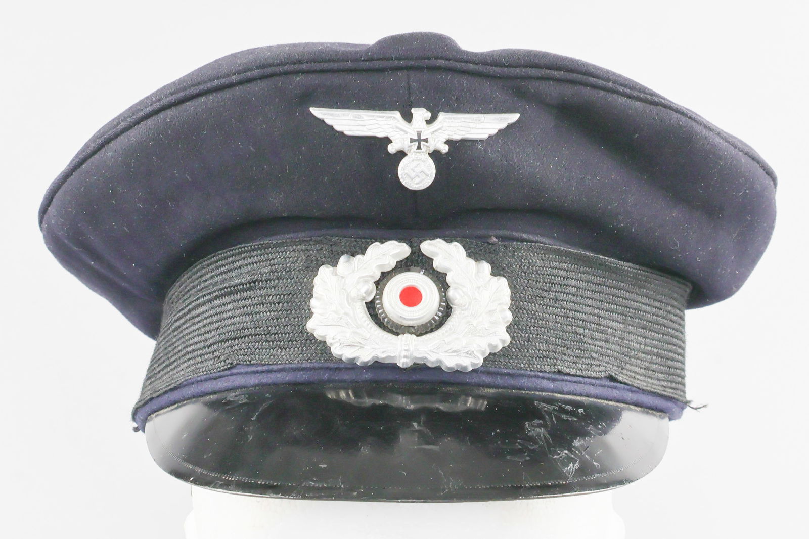 HEER VETERAN'S VISOR CAP: Visor cap worn by a veteran of service in the German Heer (Army), a navy blue wool peaked cap with a woven black side band. Shows the typical Nazi-era veteran's national eagle and swastika with