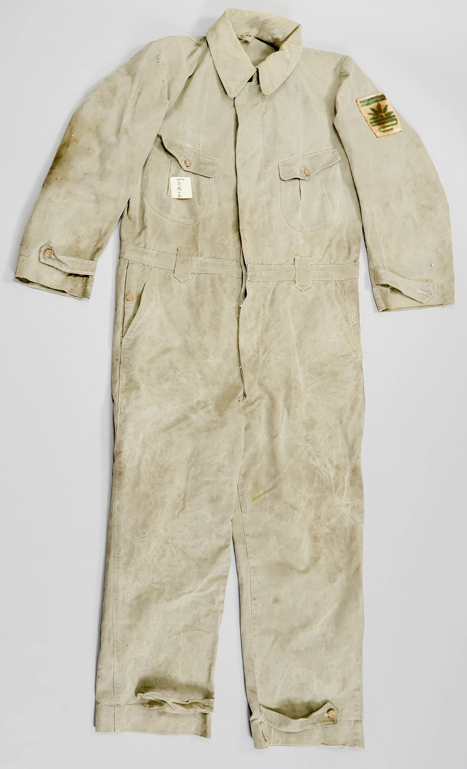IMPERIAL JAPANESE NAVY COVERALLS, ATTRIBUTED TO A SHINYO SUICIDE BOAT PILOT: A pair of World War II Imperial Japanese Navy coveralls, constructed of light olive green cotton and closed at front with nine tortoiseshell-pattern celluloid buttons in two sizes. A flap-covered