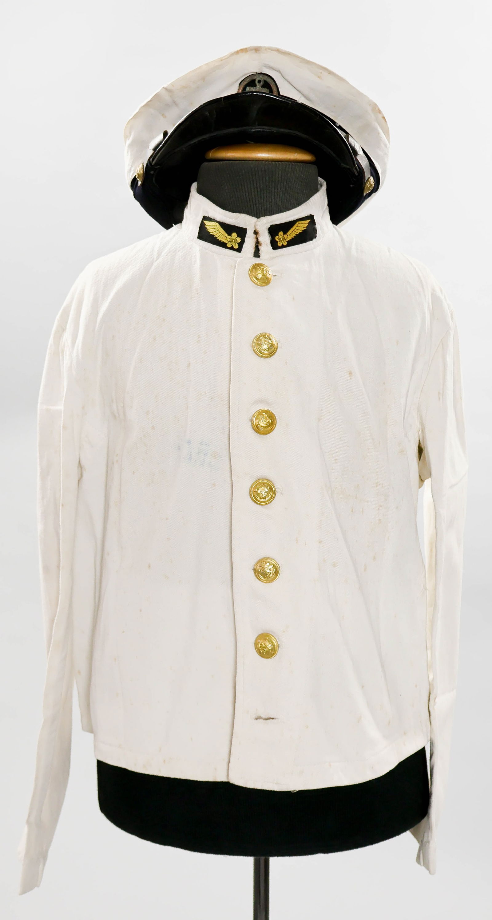 JAPANESE NAVAL AIR FORCE TUNIC AND VISOR CAP: Scarce two-piece Japanese uniform grouping. Included is a white cotton twill Japanese Naval Air Force waist-length tunic bearing a Seaman 1st Class embroidered shoulder insignia and matching trainee