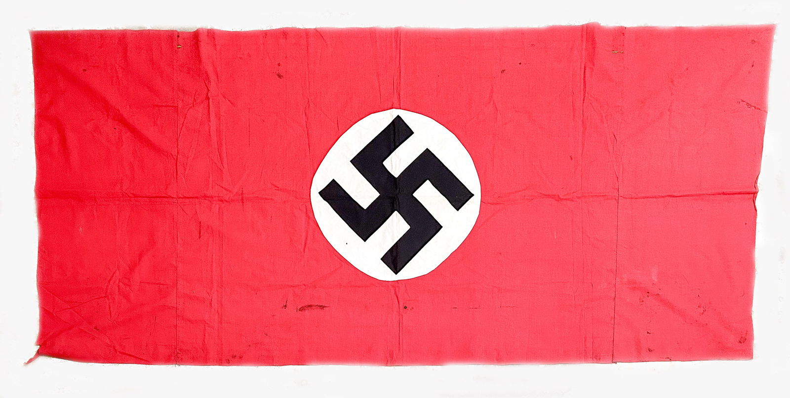 NSDAP BANNER: A red three-piece cotton or rayon NSDAP banner, 86 x 38.5 in. overall, with a sewn-on white roundel and one-piece mobile swastika at center. Curiously, two extra pieces of red fabric have been sewn