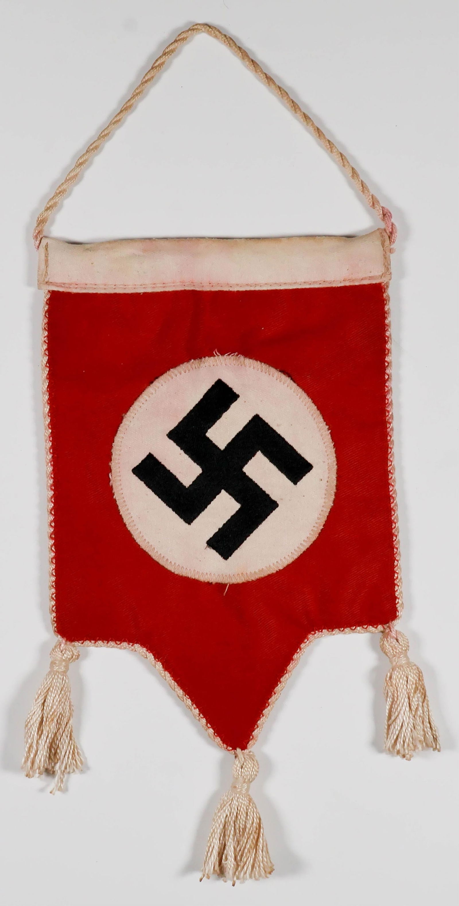NSDAP DESK FLAG: NSDAP desk flag, 9 x 5 in. overall including tassels, two-sided with separate discs with embroidered swastikas sewn on either side, with three tassels at bottom and suspension cord. Color has run
