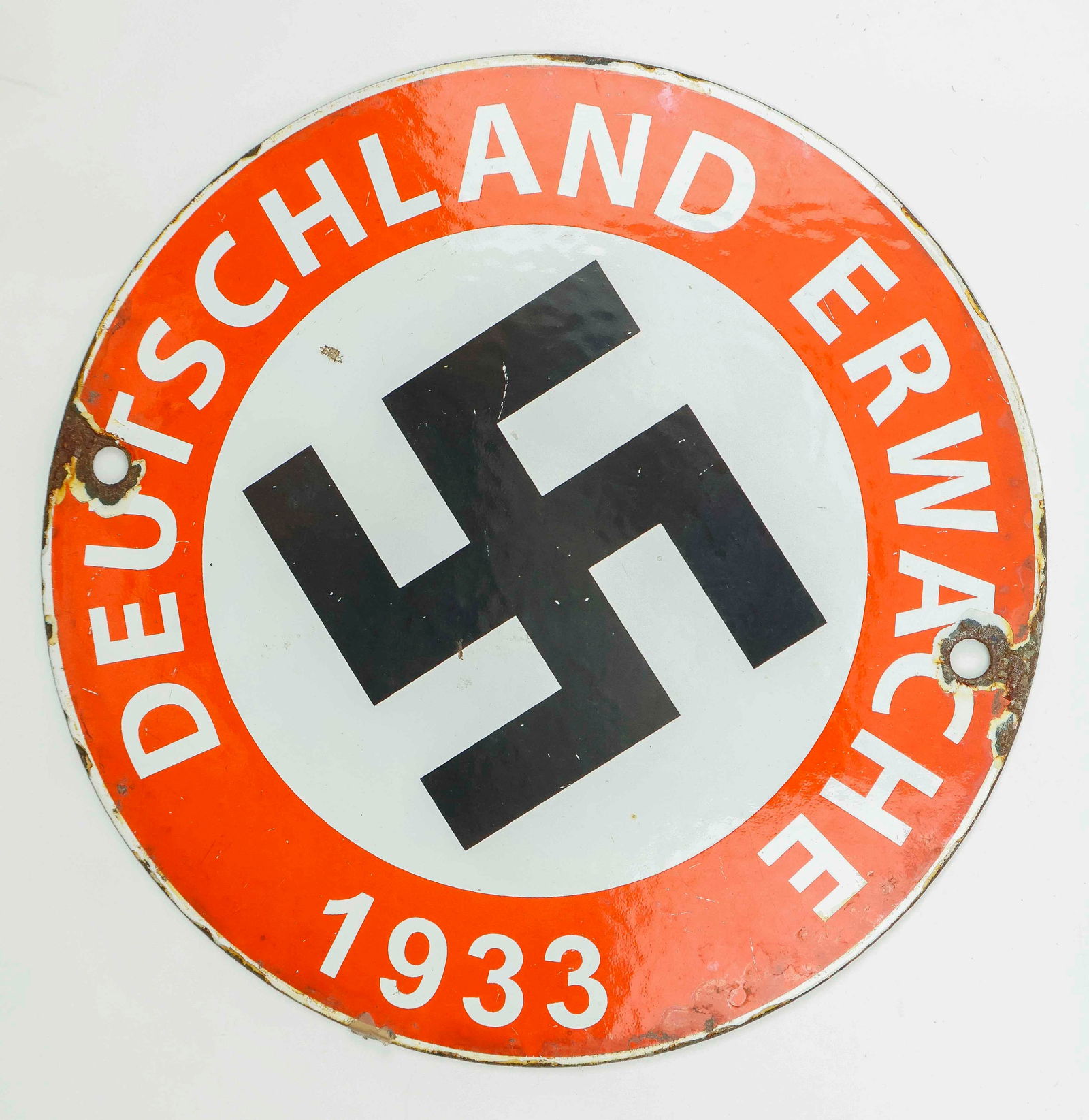 'DEUTSCHLAND ERWACHE' ENAMEL SIGN: Small circular enameled metal sign, 5.75 in. dia., reading: 'DEUTSCHLAND ERWACH 1933' about the edge on a red background, a mobile swastika on a white field at center. There are two rusted screw