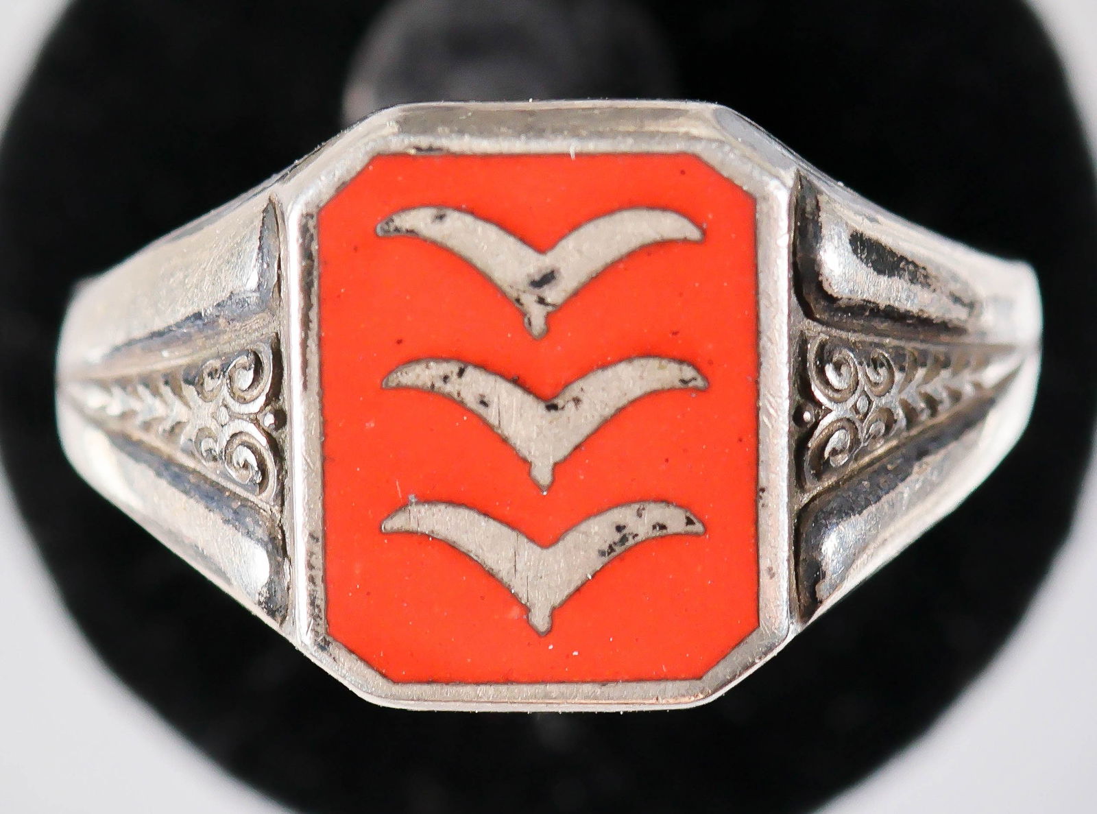 LUFTWAFFE ANTI-AIRCRAFT ARTILLERY RING: Luftwaffe anti-aircraft artilleryman's ring, unmarked but likely plated or sterling silver, the face comprised of three gull wings, a feldwebel's rank on a red enameled background, the sides of the