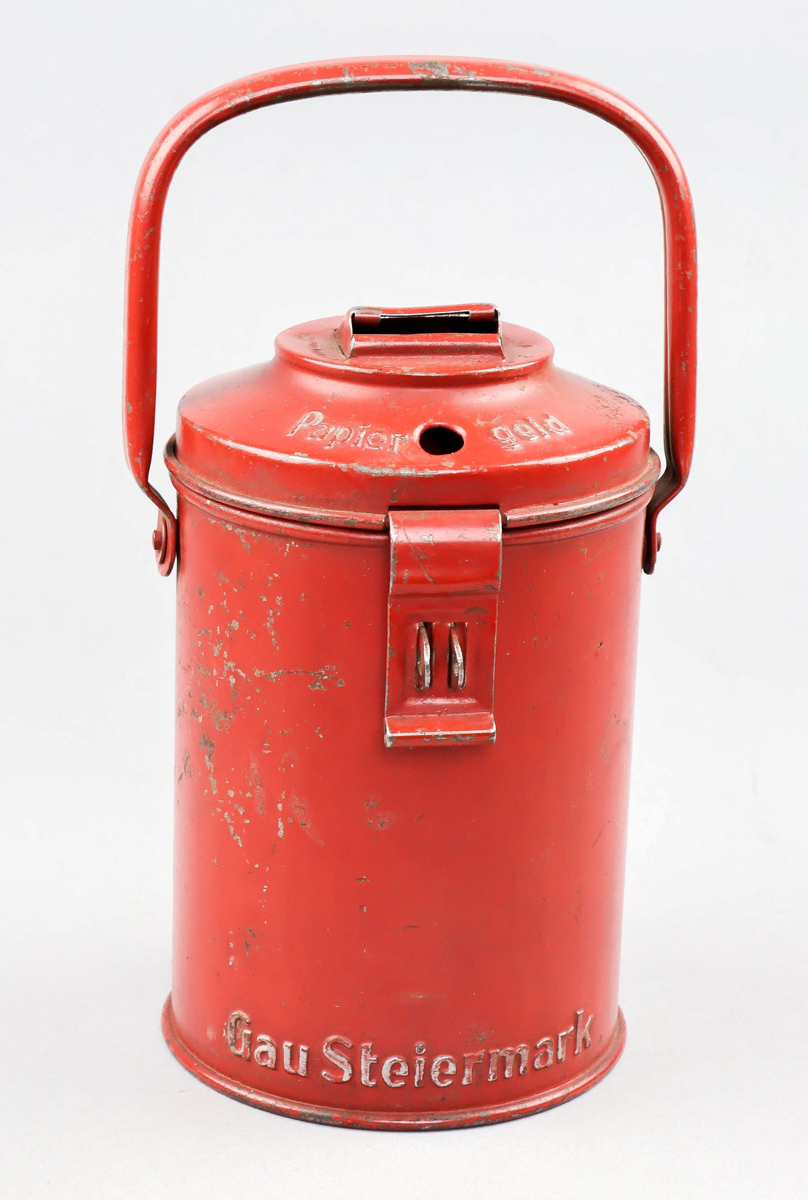 WINTERHILFSWERK COLLECTION CAN: Scarcer Gau-issued Winterhilfswerk collection can, red-painted steel 7 in. tall and made by M. Westermann & Co. Bas relief test includes 'Gau Steiermark' at bottom, 'Papier geld' near a hole to