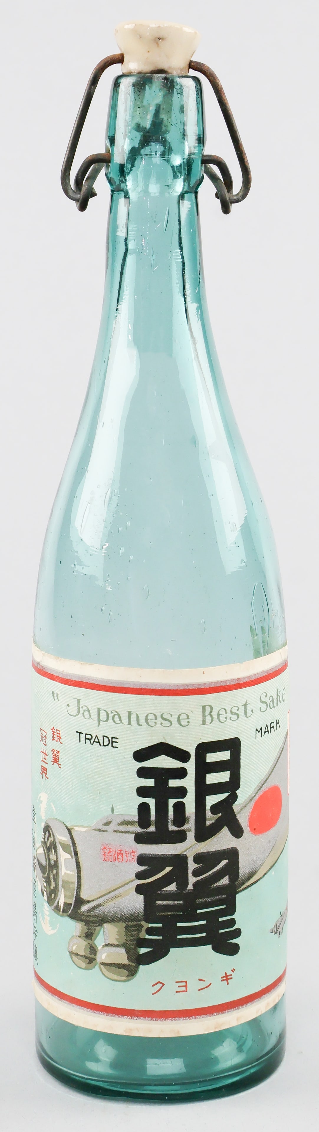 JAPANESE 'ZERO' SAKE BOTTLE: Japanese World War II 'Silver Wings' sake bottle, approx. 12.5 in. tall aqua green crudely made glass with ceramic stopper. The 6 x 4.5 in. label pictures two Japanese 'Zero' fighters in flight with