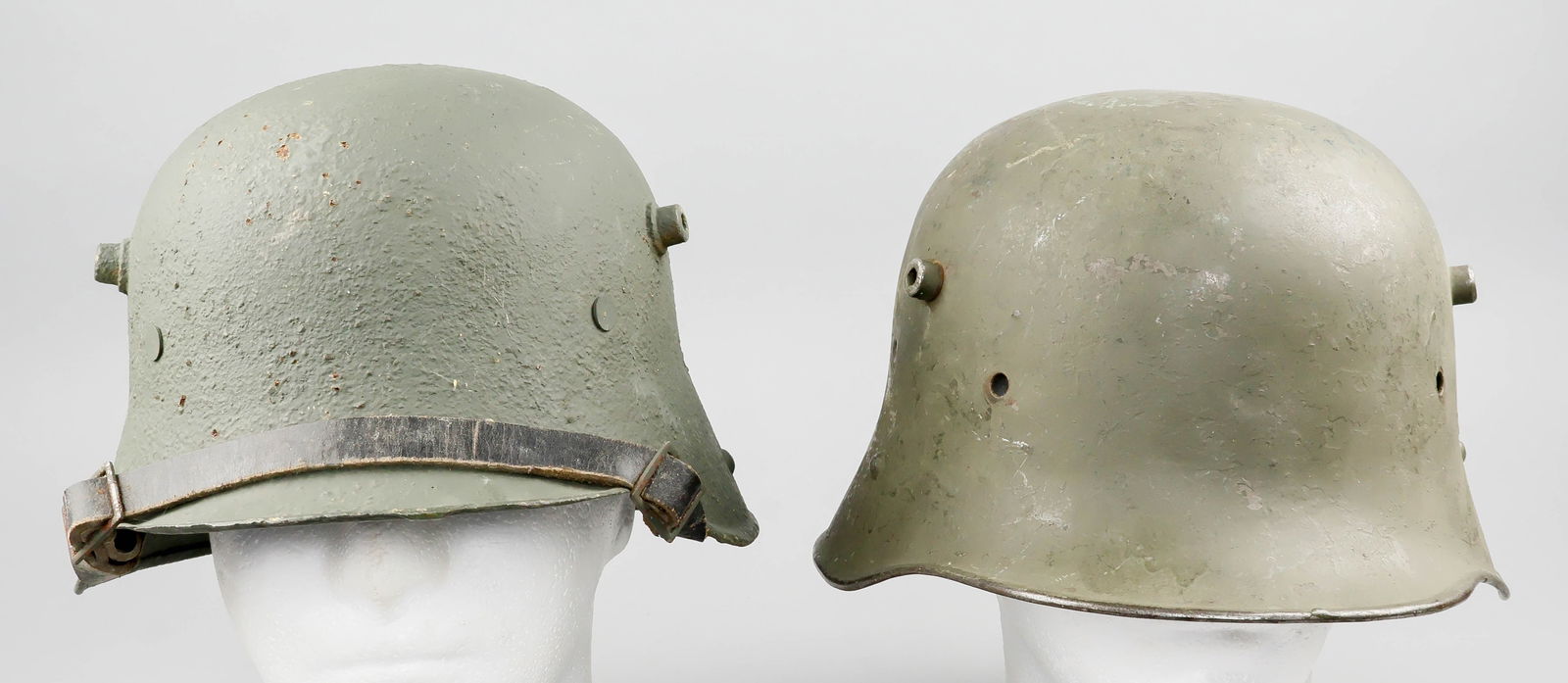 RELIC 'STAHLHELM' COMBAT HELMET SHELLS (2): A good pair of relic condition 'Stahlhelm' helmet shells, the first an Austrian M17, repainted olive green overall, retaining strap lugs but with no markings present, with extra holes drilled between