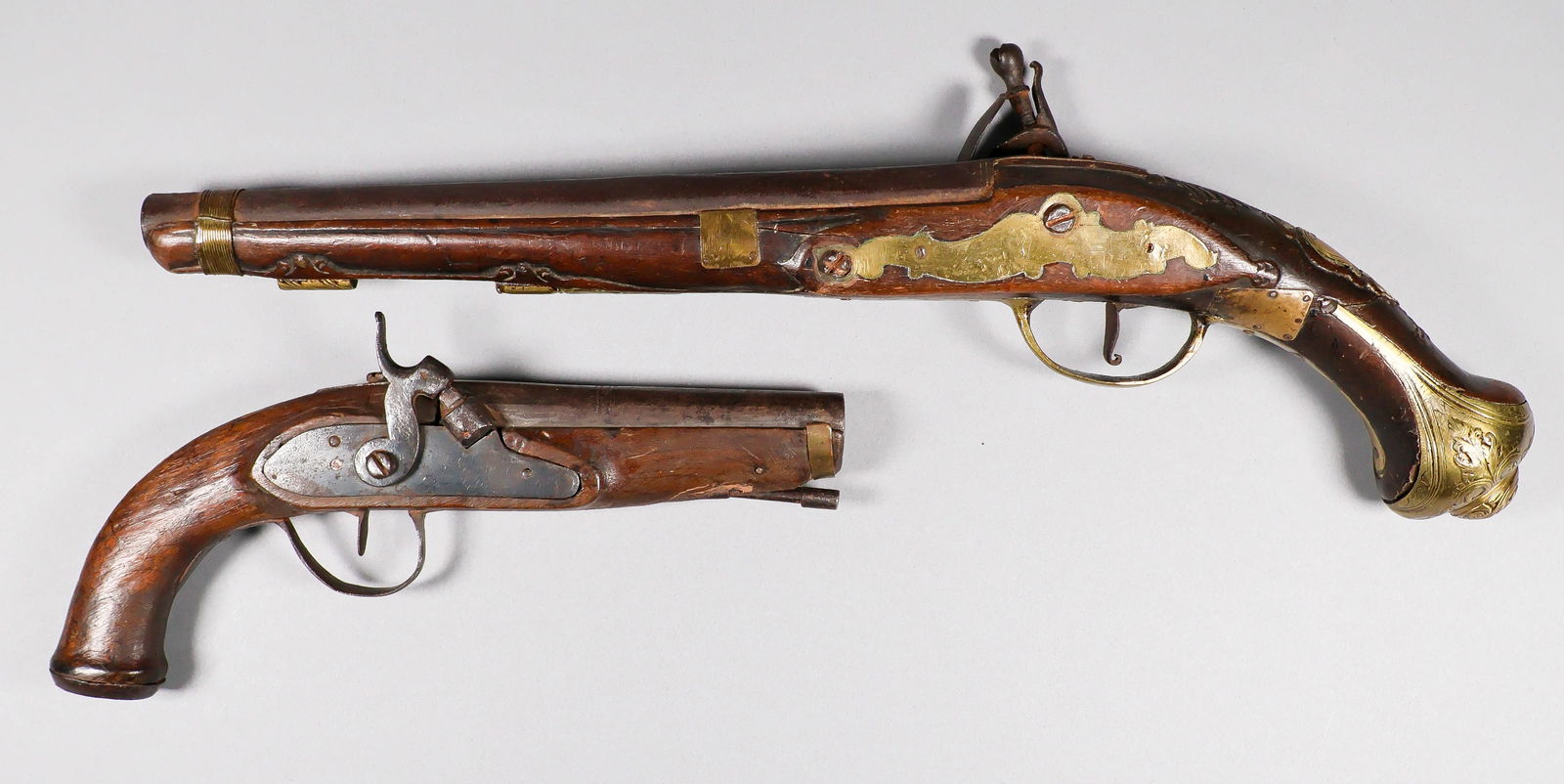 ANTIQUE SINGLE-SHOT PISTOLS (2): A nice pair of antique single-shot ‘wall-hanger’ pistols, the first with a flintlock action and brass butt, trigger guard, sideplate, cartouche plate and cleaning rod loops, 9.75 in.