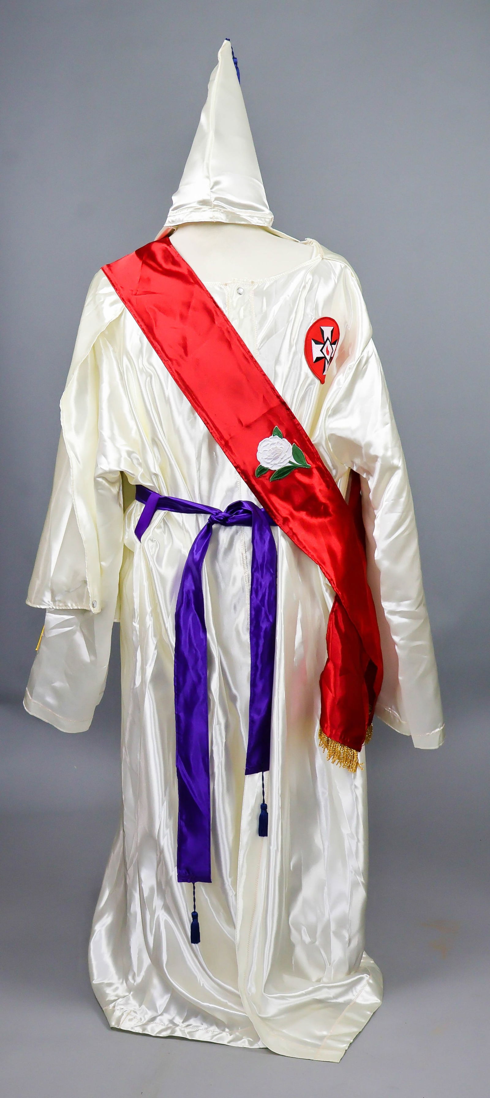 KU KLUX KLAN ROBE, HOOD AND SASH: Later ca. 1960’s-70’s Ku Klux Klan robe and hood, both constructed of white satin-finish rayon, the robe featuring a nylon ‘Knights of Kamellia’ patch on the left breast, with