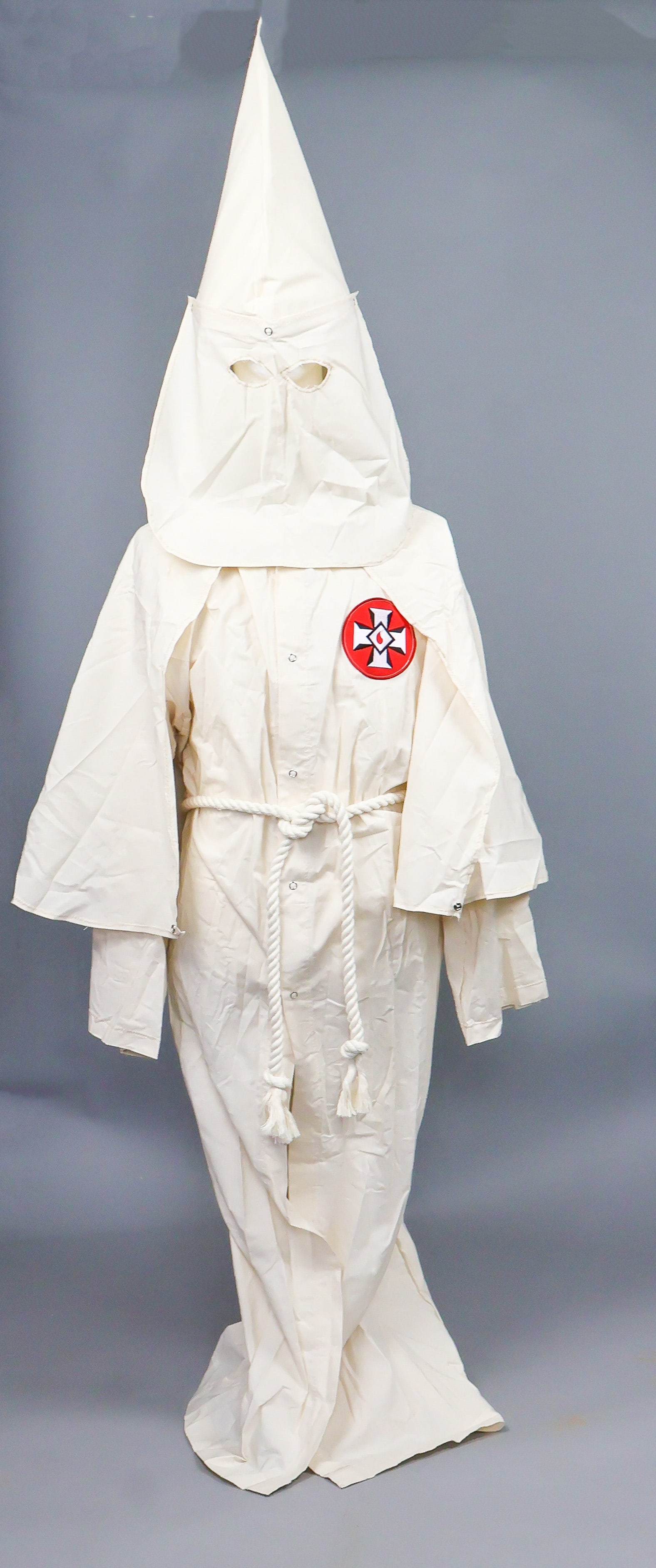 KU KLUX KLAN ROBE AND HOOD: Entirely typical ca. 1960’s-70’s Ku Klux Klan robe and hood, both constructed of white cotton, the robe featuring a nylon ‘Knights of Kamellia’ patch on the left breast. The