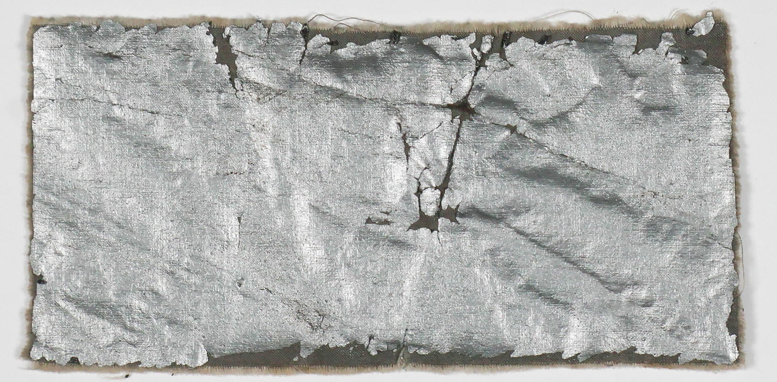 LZ-127 GRAF ZEPPELIN ENVELOPE RELIC: A section of cotton fabric, 4 in. x 2 in., painted with aluminum-impregnated aircraft dope attributed to the outer skin of the pioneering German airship LZ-127 GRAF ZEPPELIN. The relic was likely