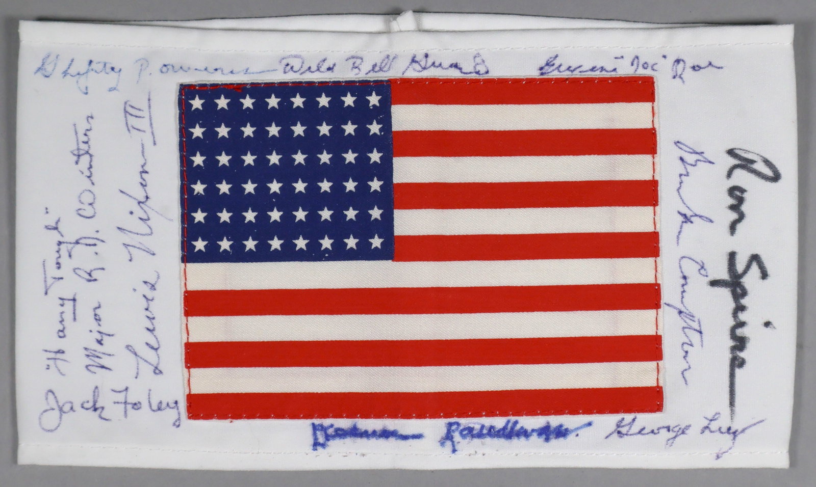 BAND OF BROTHERS: A souvenir white cloth armband bearing a patch of the American flag, signed by 10 members of the 502nd P.I.R., 101st Airborne: RICHARD ‘DICK’ WINTERS, LEWIS NIXON III, DENVER RANDLEMAN,