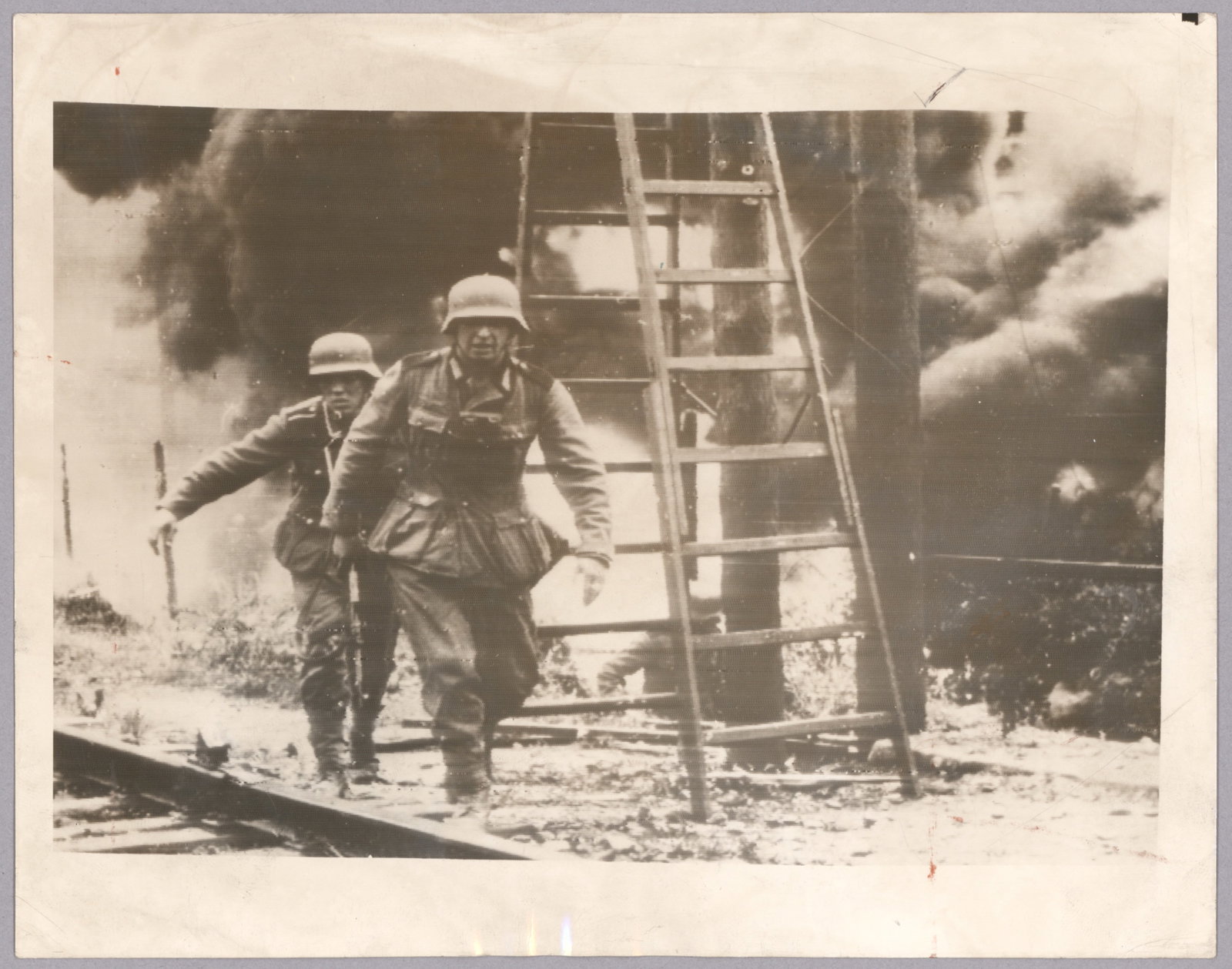 NOTED IMAGE OF GERMANS ADVANCING IN BURNING RUSSIAN TOWN: Exceptional original Acme period press photograph, 9 x 7 in. b/w, a well known image of German soldiers advancing within a burning city or town in Russia. Verso bears a stamp from Acme, printed