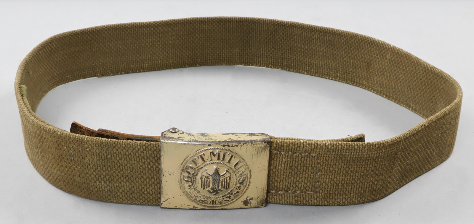 AFRIKA KORPS 'GOTT MIT UNS' BUCKLE WITH BELT: A well-worn painted belt buckle with corresponding Afrika Corps canvas belt. The leather strap affixed to the buckle is stamped ‘Kuernberg 1941’. Although the buckle exhibits legitimate